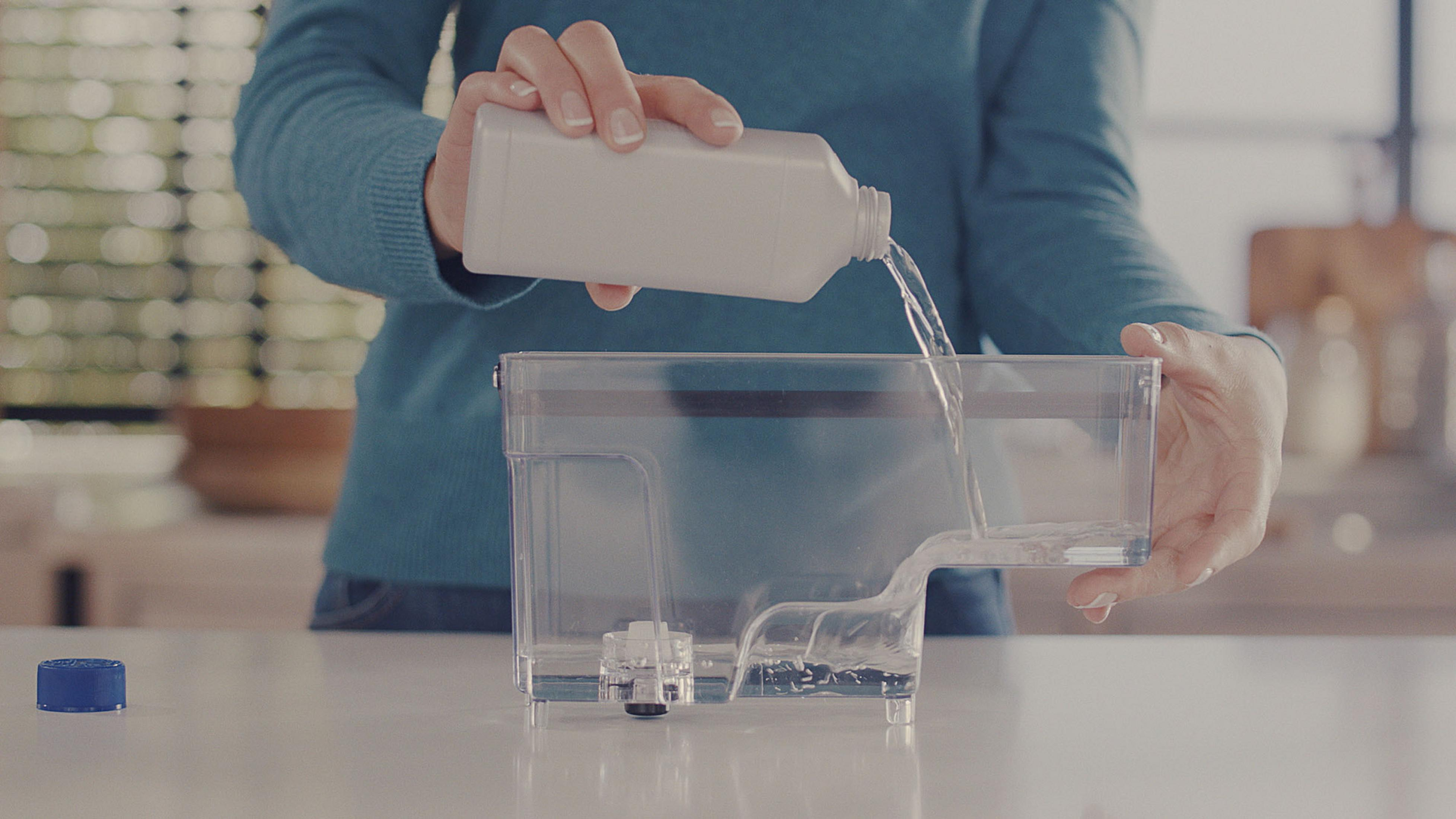 Eine Person gießt Wasser in einen transparenten Behälter.