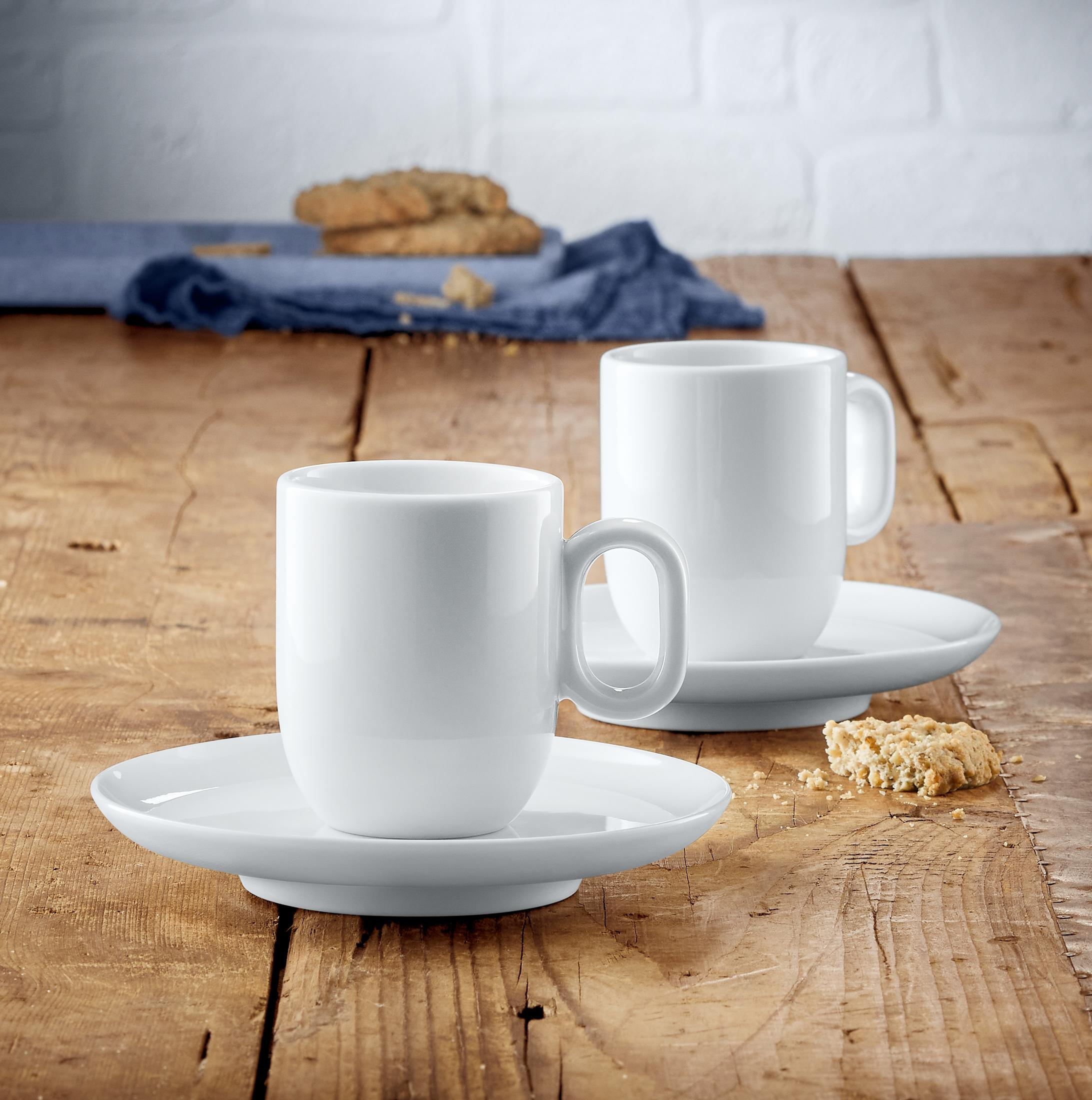 Zwei weiße Kaffeetassen mit Untertassen auf einem Holztisch. Es gibt Kekse.