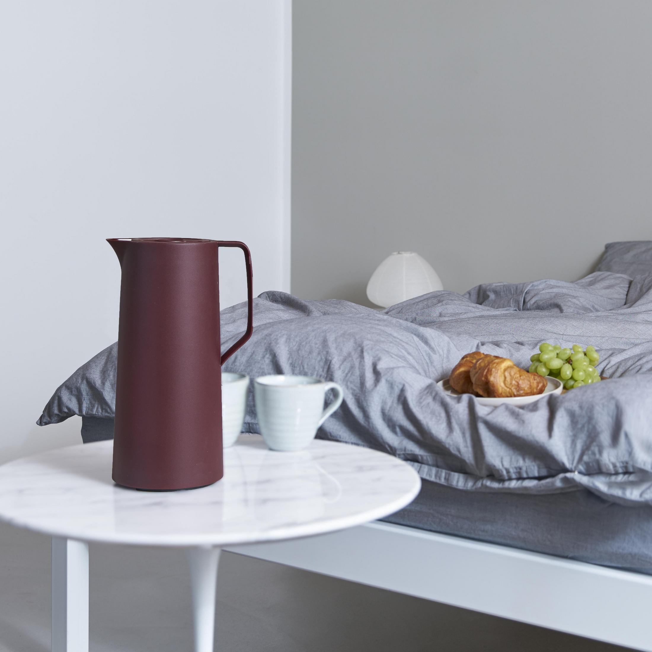 Schlafzimmer mit einem weinroten Krug, zwei Tassen, einem Teller mit Essen und einem Bett.