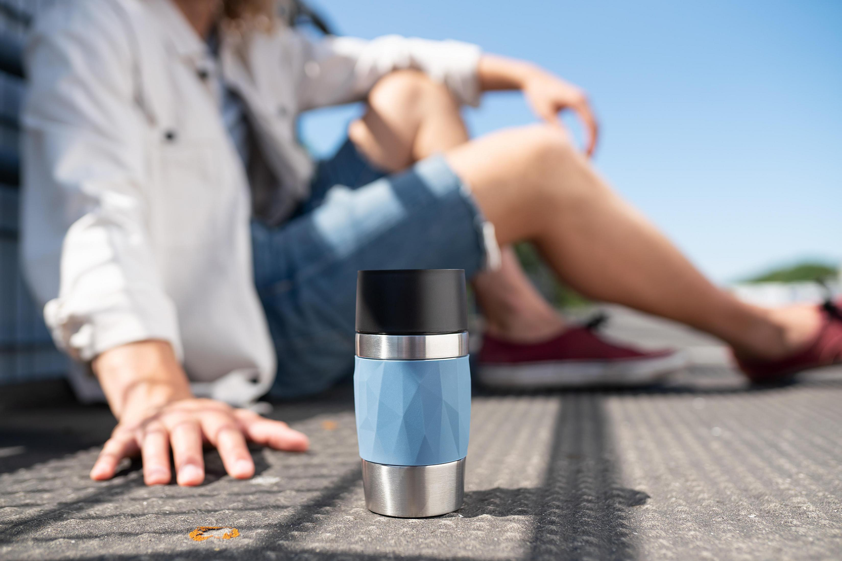 Eine Person sitzt auf dem Boden mit einem blau-silbernen Becher.