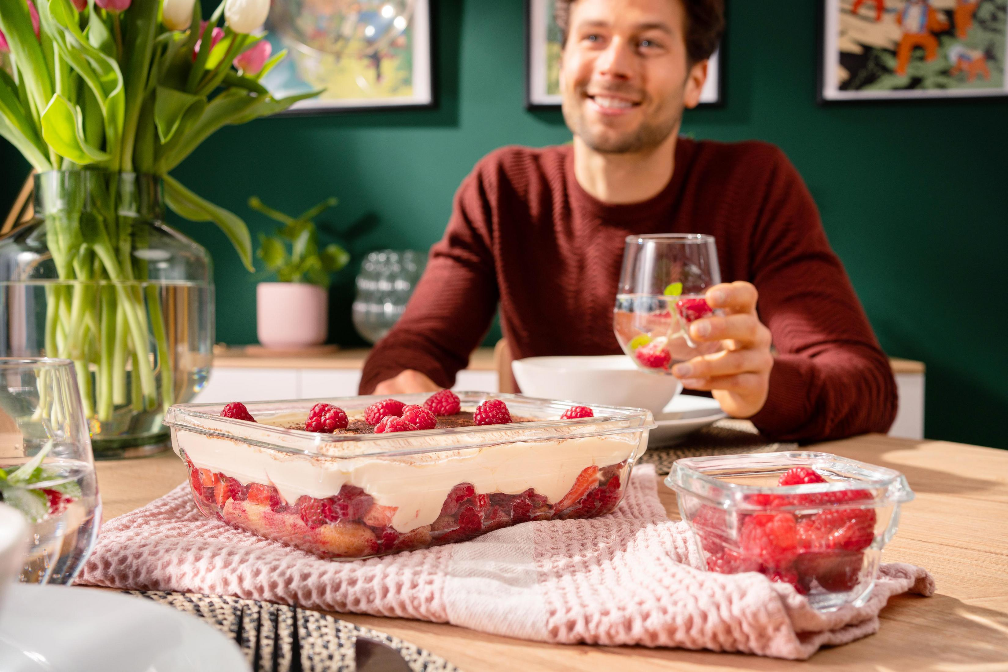 Mann am Tisch mit Essen. Tiramisu und Himbeeren in Glasbehältern, Tulpen in Vase.