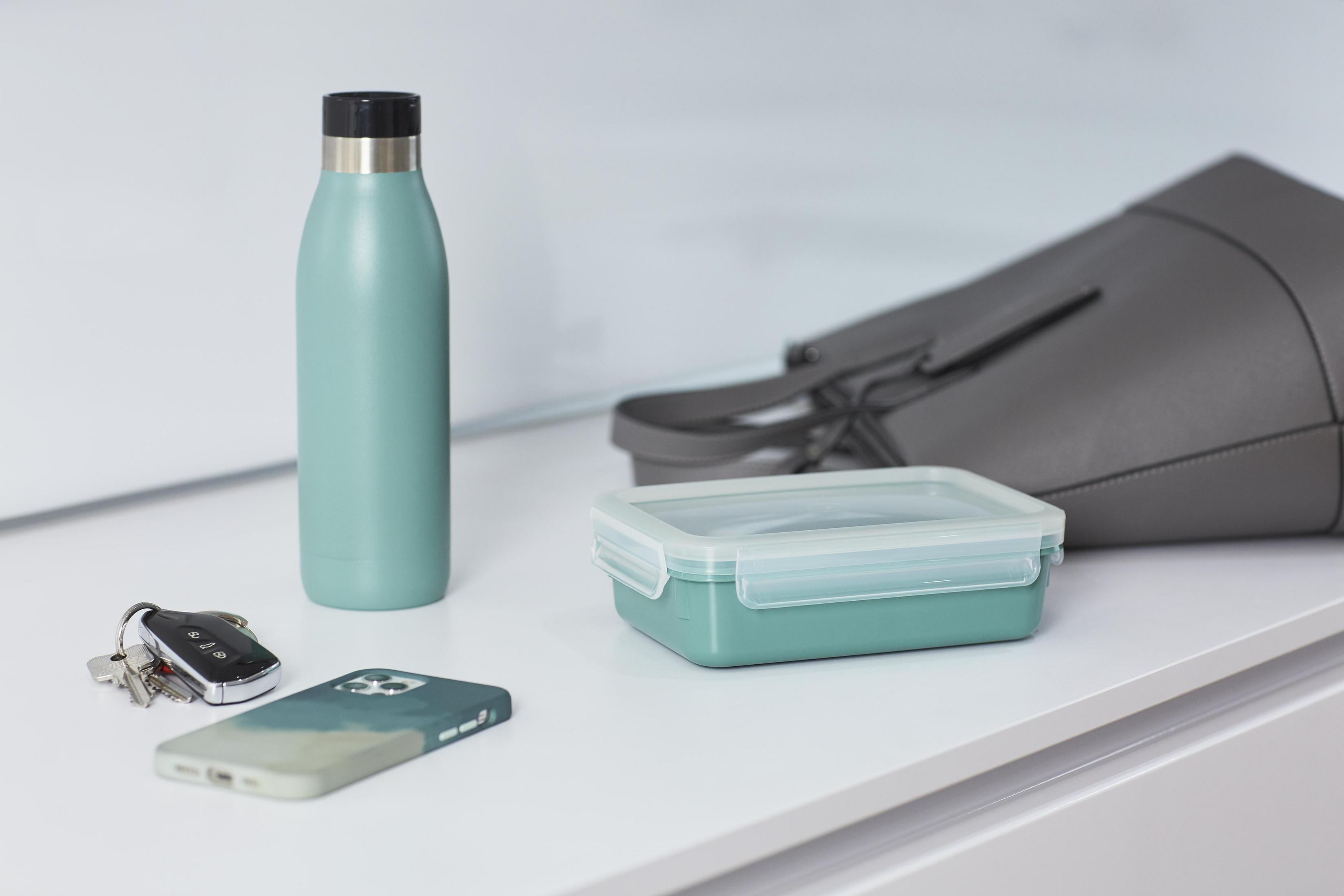 Eine türkisfarbene Brotdose, Wasserflasche, Telefon, Schlüssel und Tasche auf weißer Oberfläche.