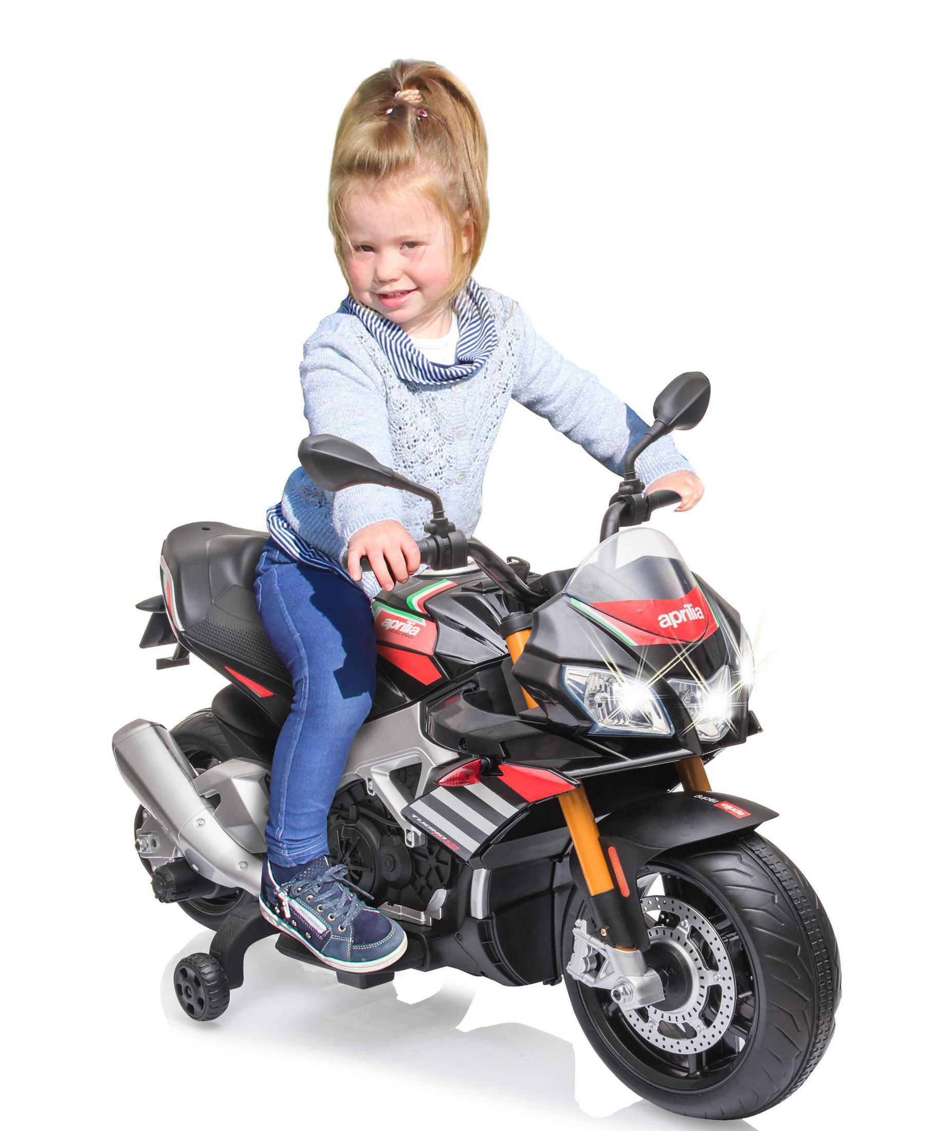 Un niño pequeño sentado en una moto de juguete. Es roja y negra, con ruedines.