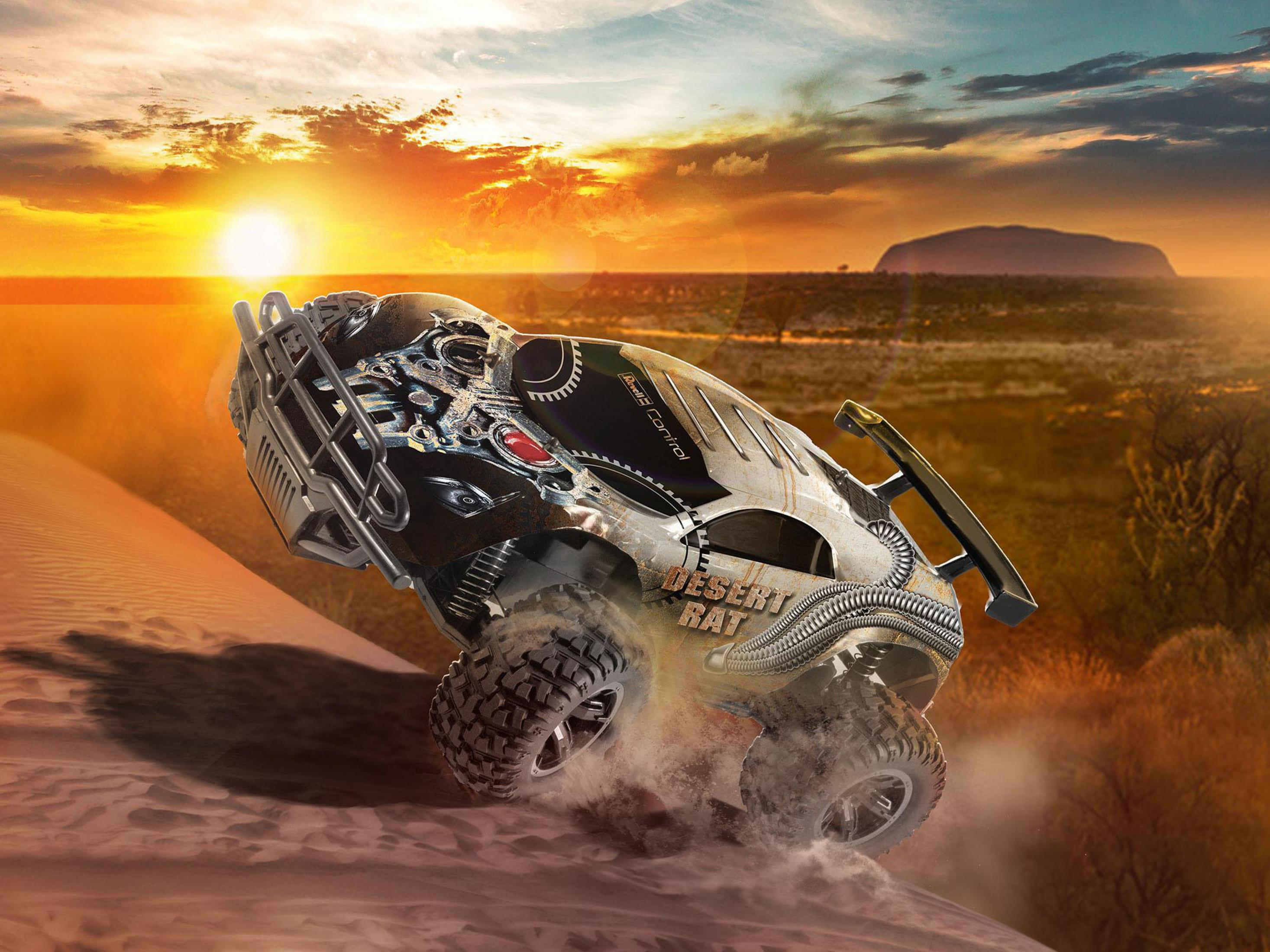 Ein Spielzeug-Geländewagen springt über eine Sanddüne vor einem Sonnenuntergang mit Uluru im Hintergrund.