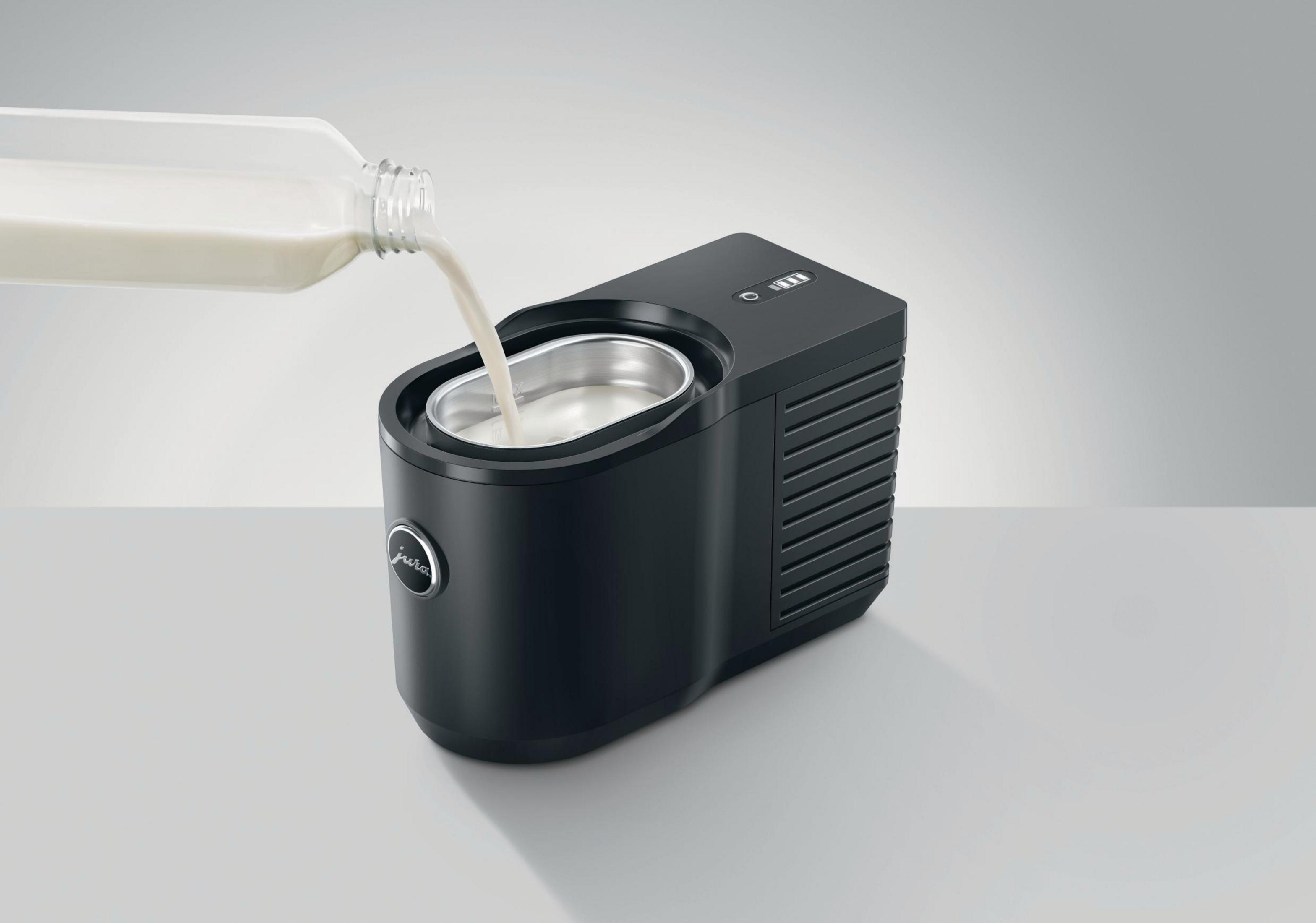 Espumador de leche negro con leche vertiéndose de una botella. La máquina tiene un panel de control.
