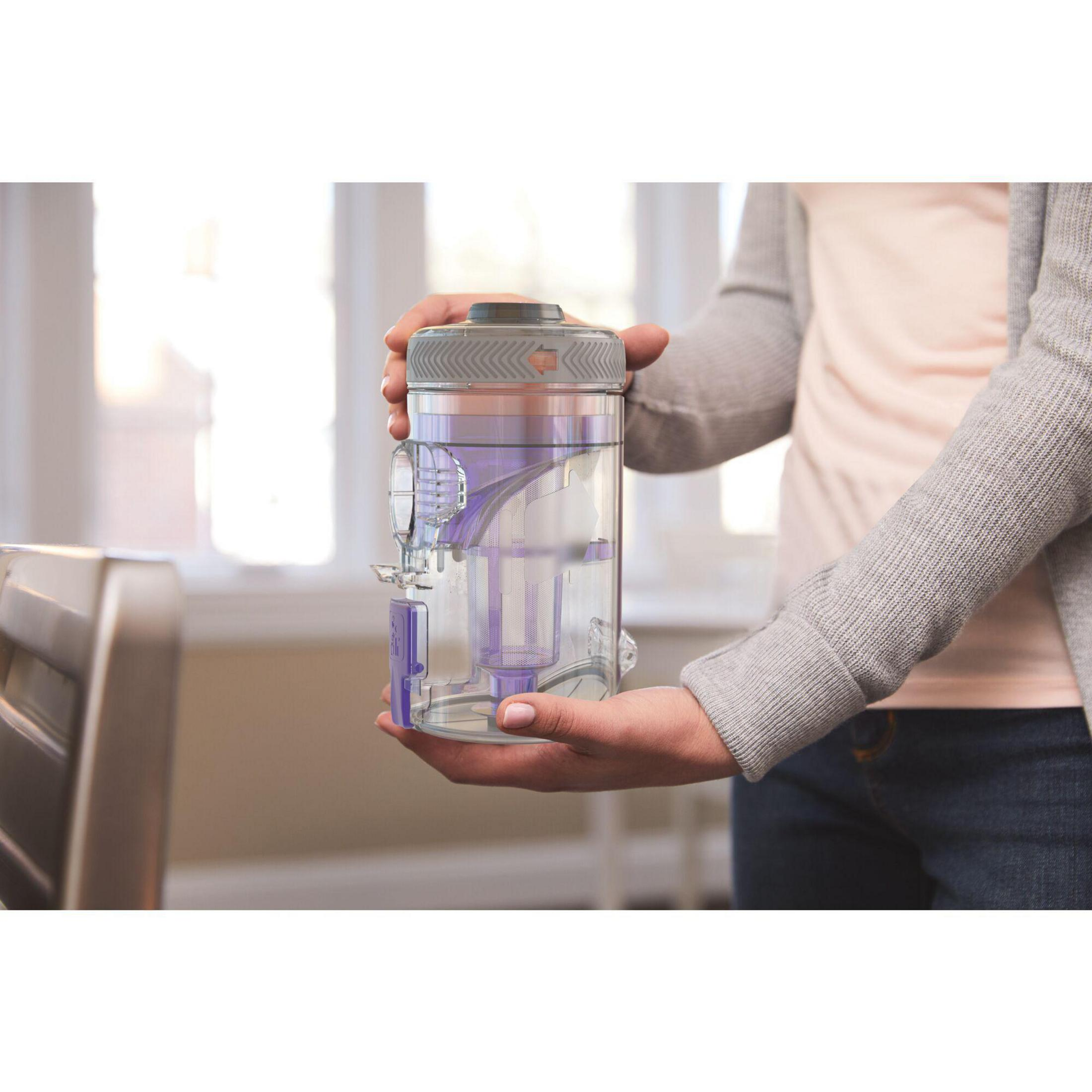 Kobieta trzyma pojemnik na wodę do odkurzacza. Pojemnik jest szary i przezroczysty.