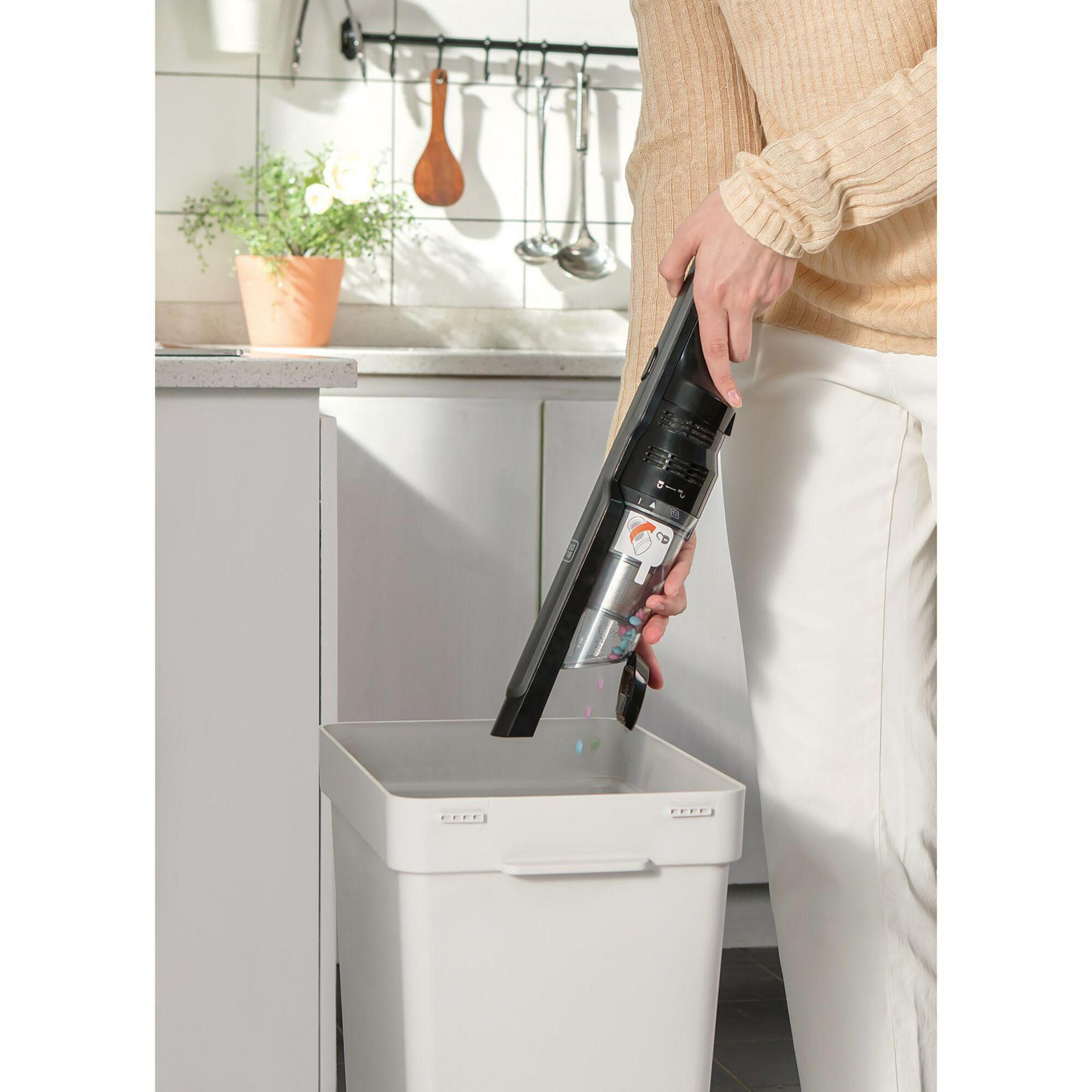 Persona vaciando una aspiradora de mano en un cubo de basura en la cocina.