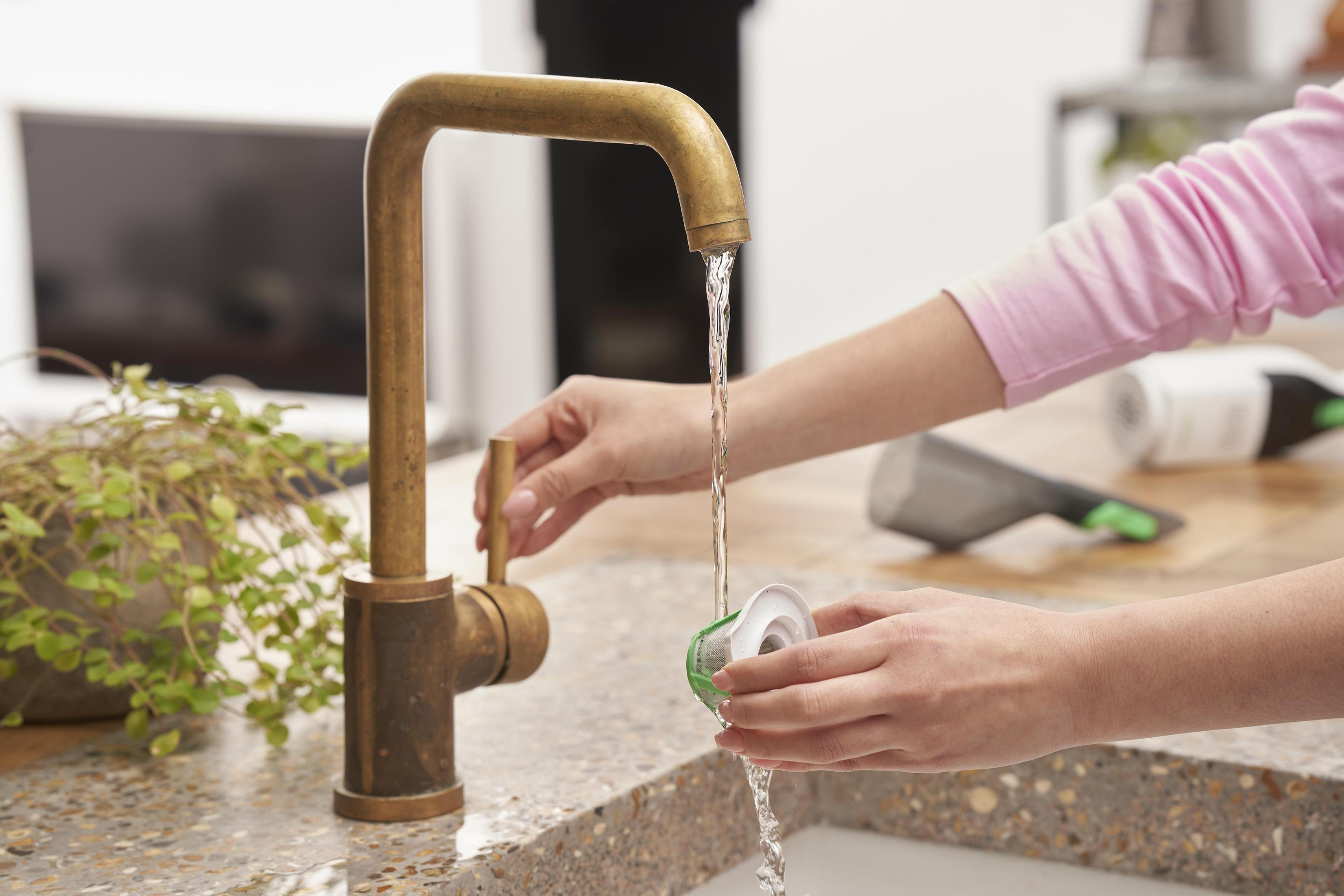 Les mains d'une personne près d'un robinet en laiton, remplissant un récipient d'eau.