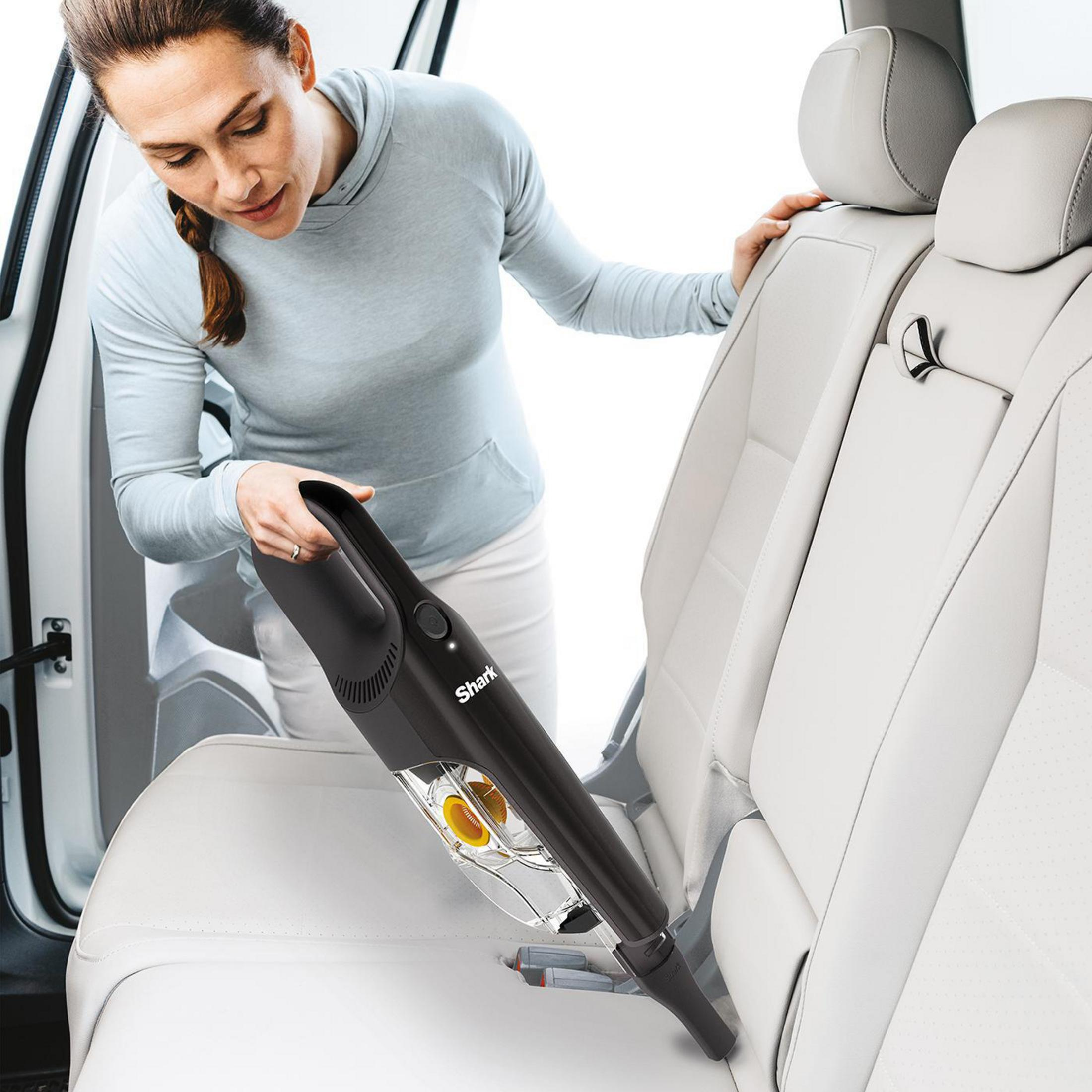 Frau, die den Autositz mit einem Shark-Handstaubsauger absaugt. Weißes Autointerieur.