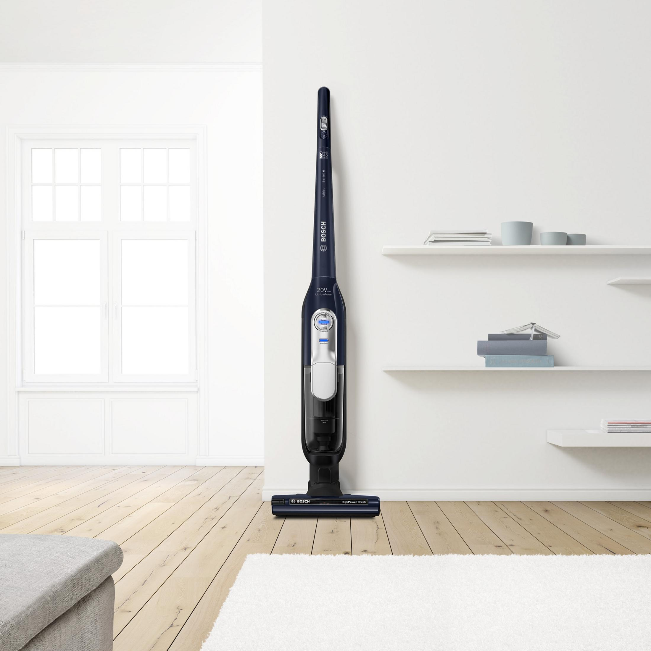 Aspirapolvere senza fili blu e nero in una stanza bianca, pavimento in legno chiaro.