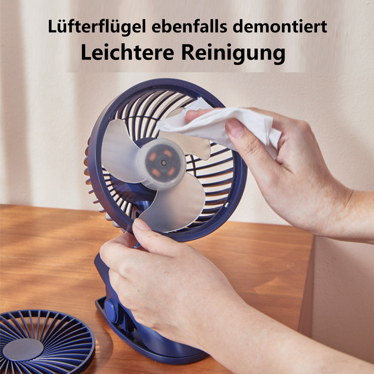 Eine Person reinigt einen blau-silbernen Ventilator. Der Ventilator steht auf Holz.