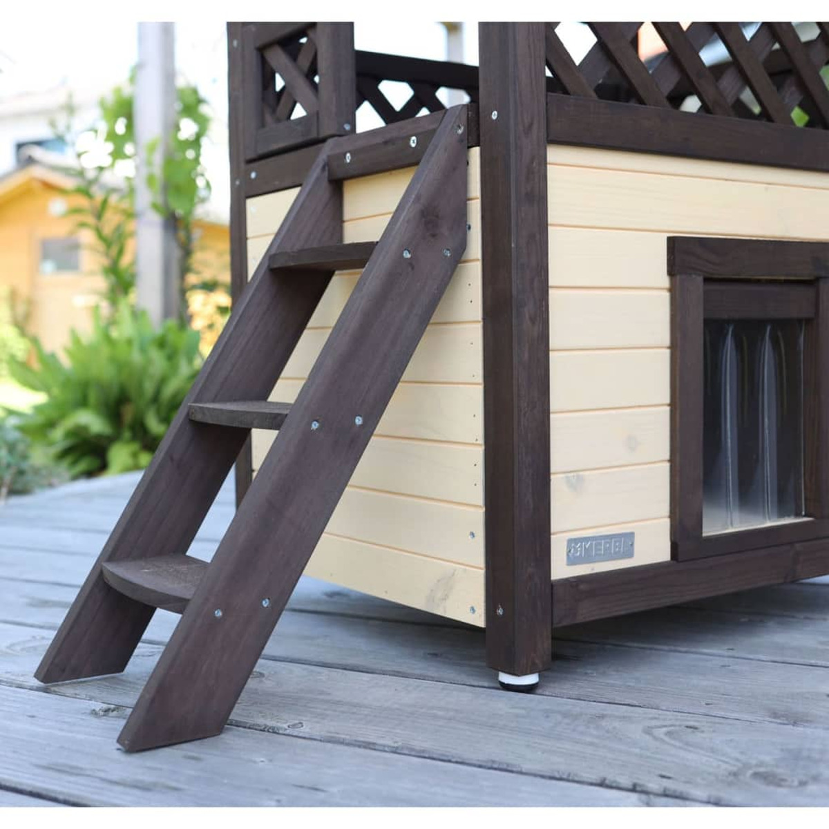 Una caseta de perro de madera con una escalera. Es marrón y beige con una ventana pequeña.