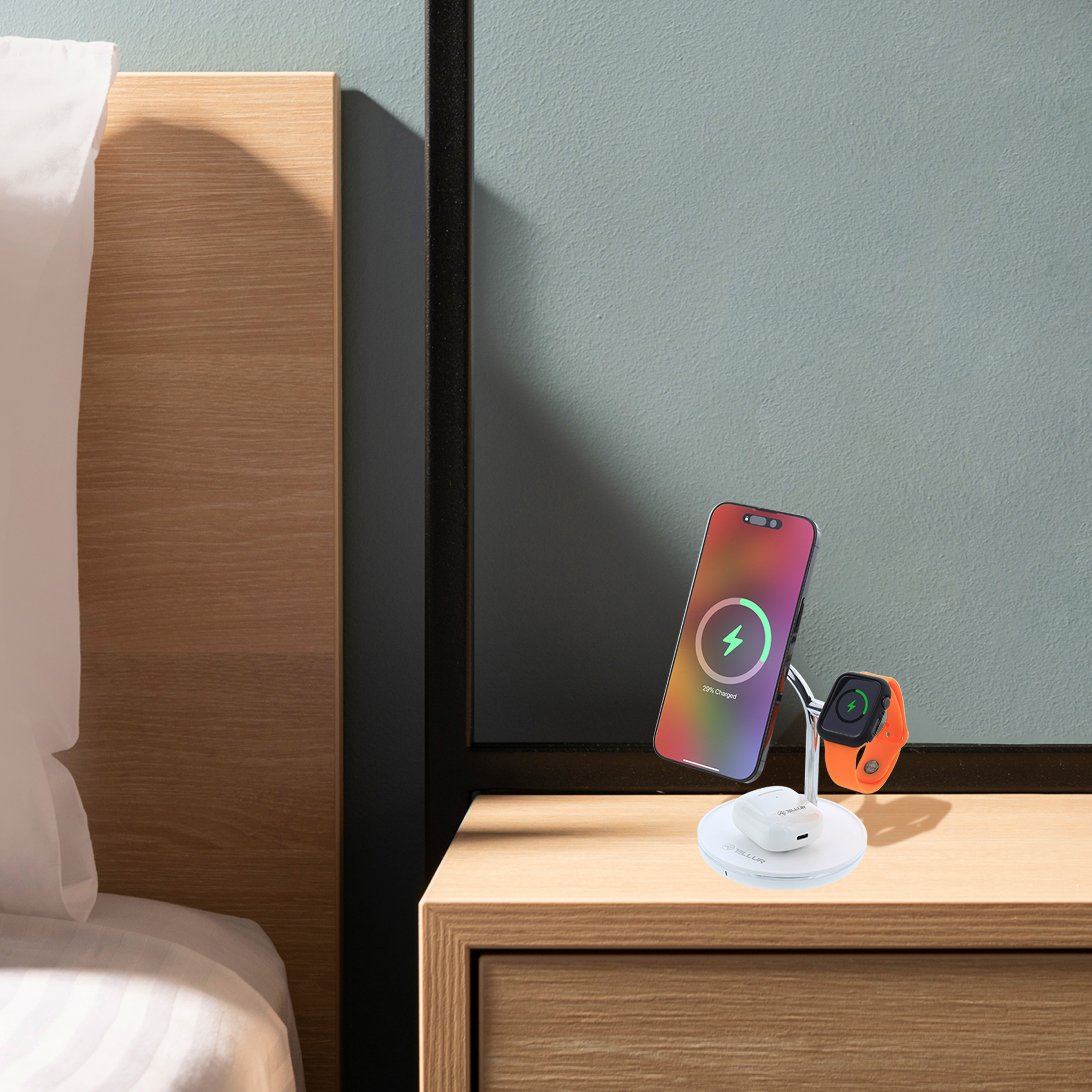 Telefon i zegarek ładują się na stoliku nocnym. Łóżko i ściana w tle.