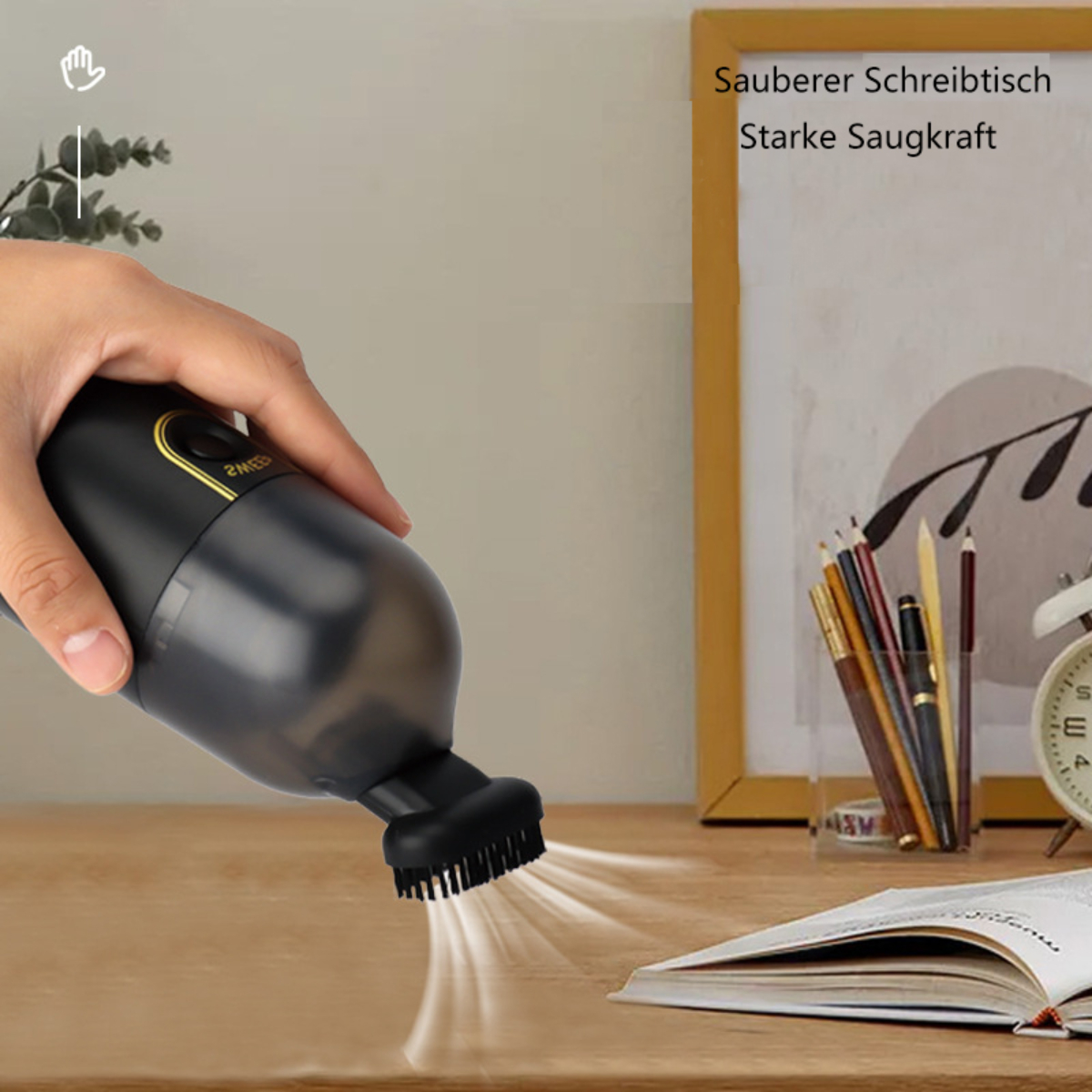 Hand hält einen schwarzen Staubsauger über einem Schreibtisch mit deutschem Text.