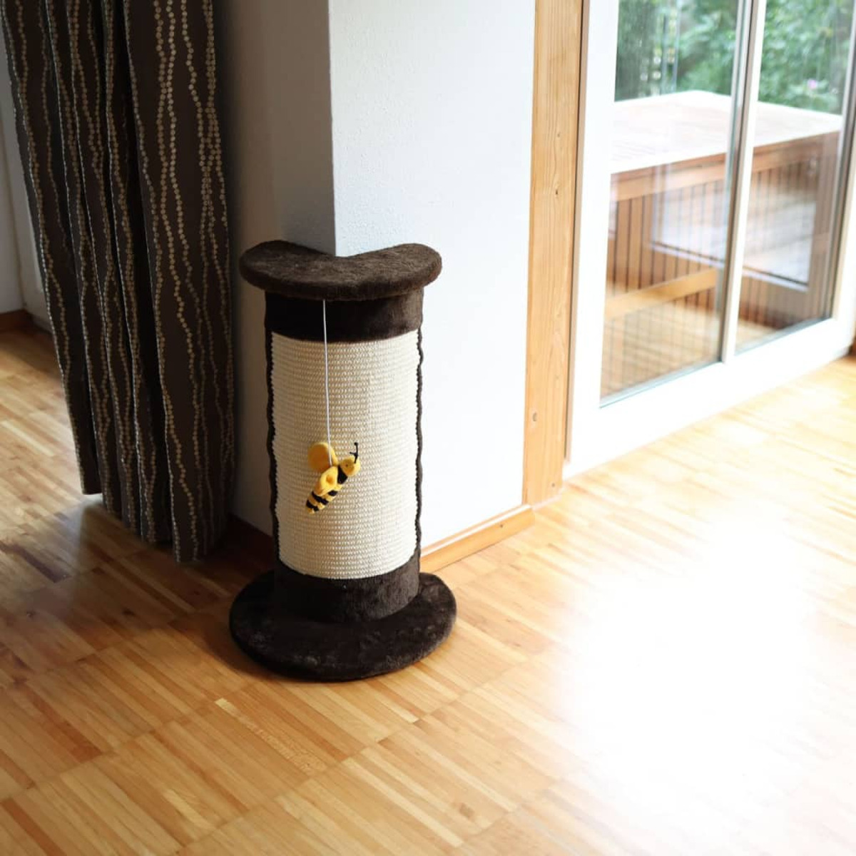 Un rascador para gatos con un juguete colgante sobre un piso de madera.