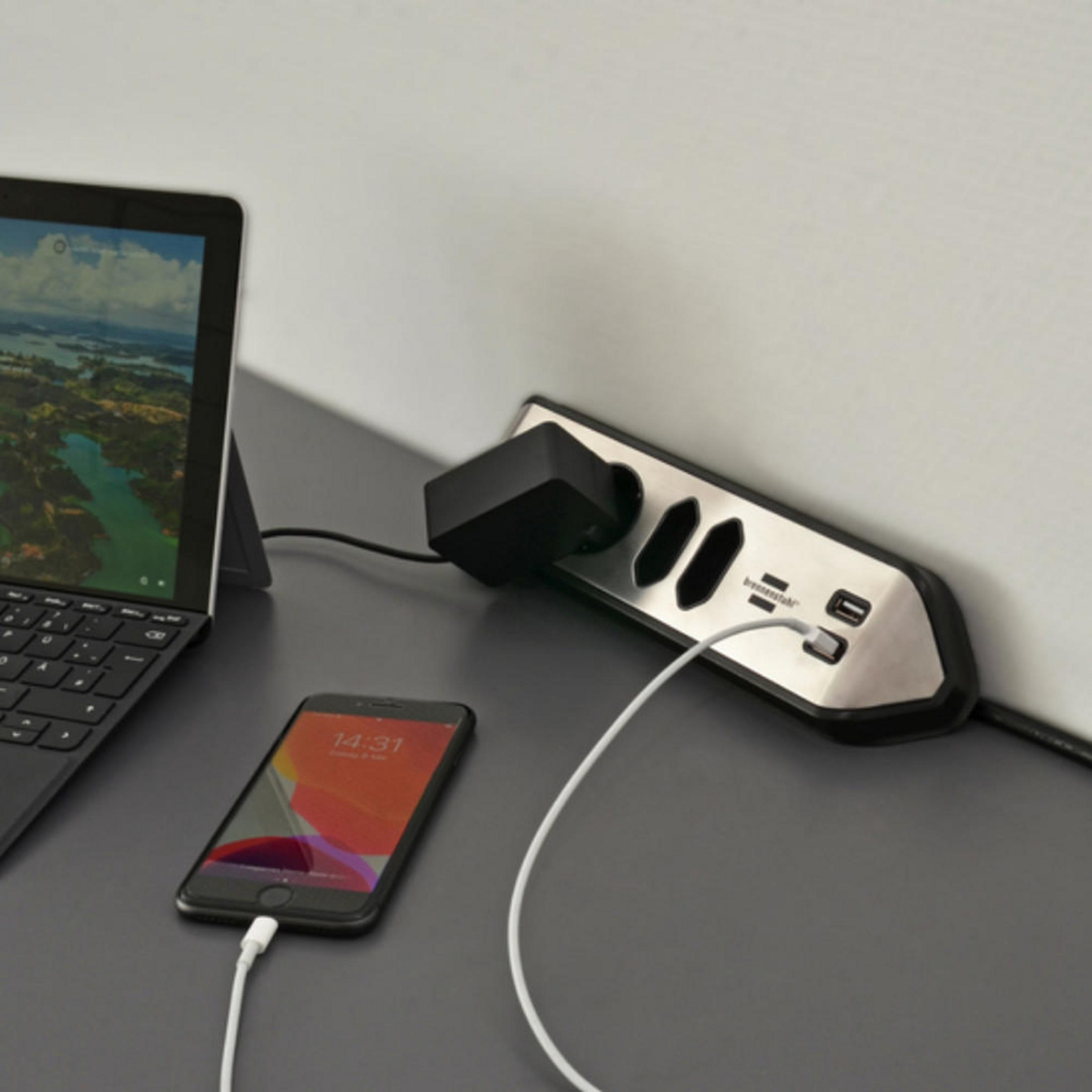 Steckdosenleiste mit Telefon und Laptop. Schwarzes Telefon mit weißem Ladekabel.
