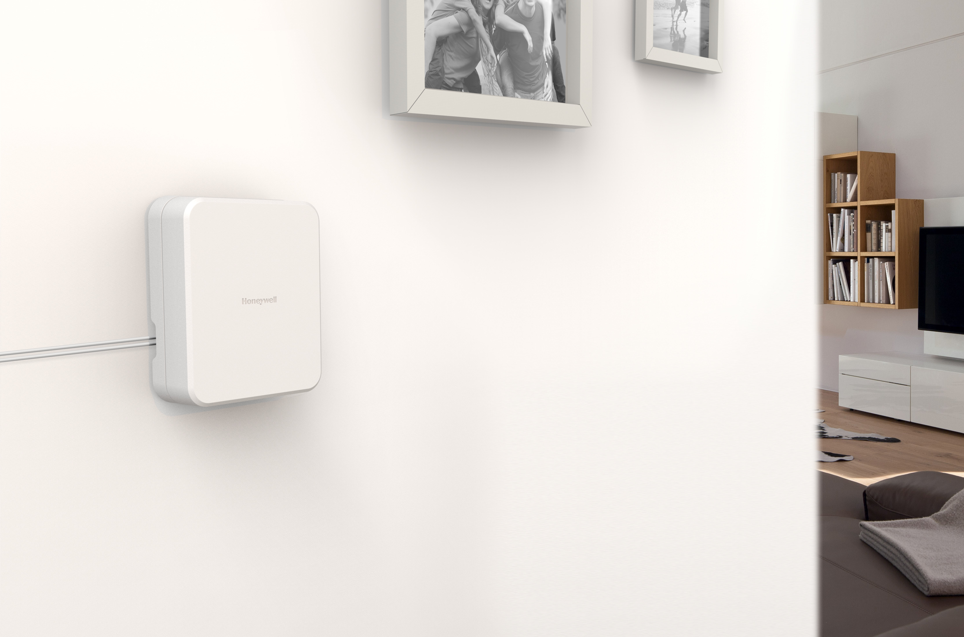 Weißes Gerät an einer Wand. Vordergrund: Gerät an der Wand. Hintergrund: Innenraum mit Bildern.