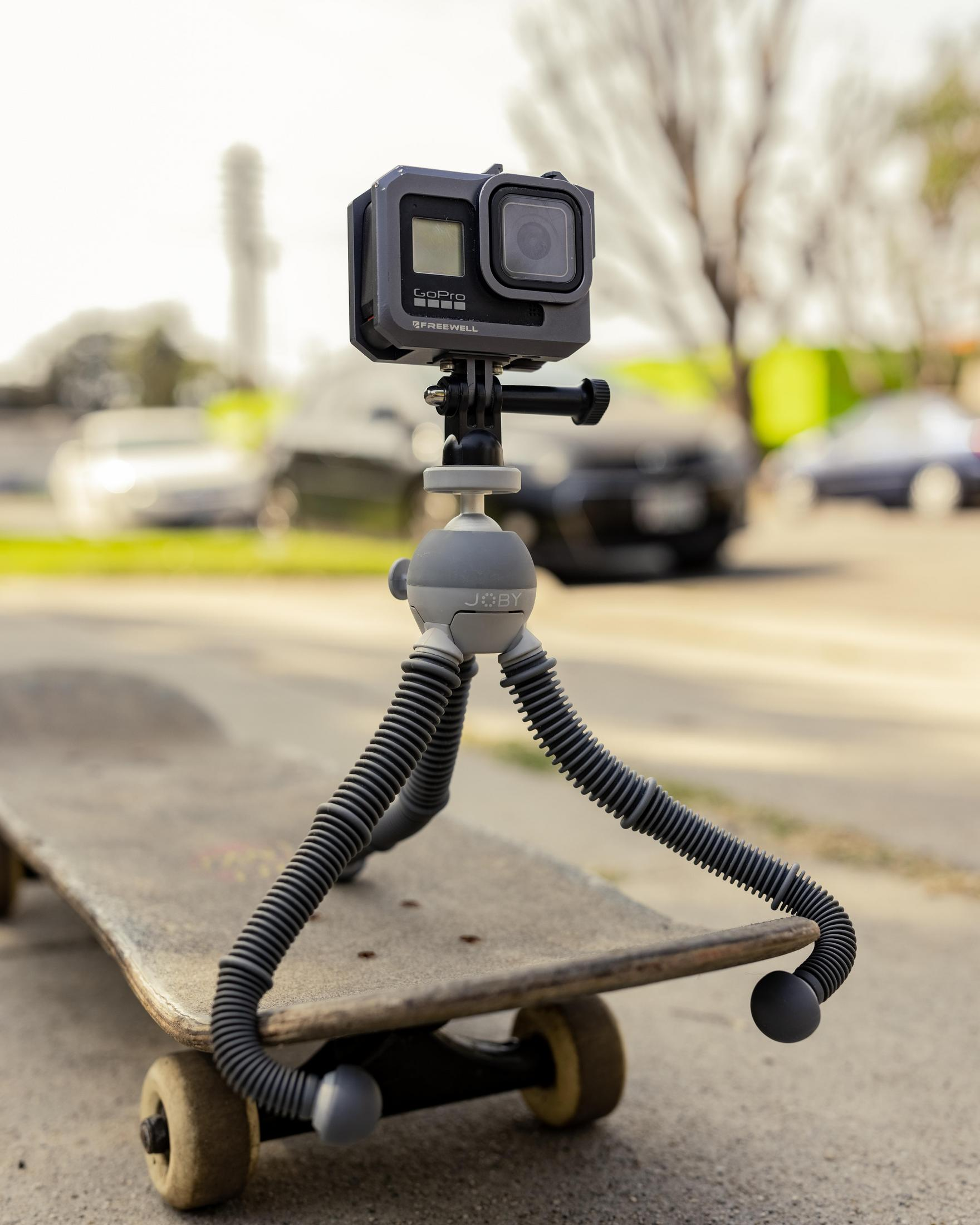 Caméra GoPro sur un trépied fixé à un skateboard, sur un trottoir.