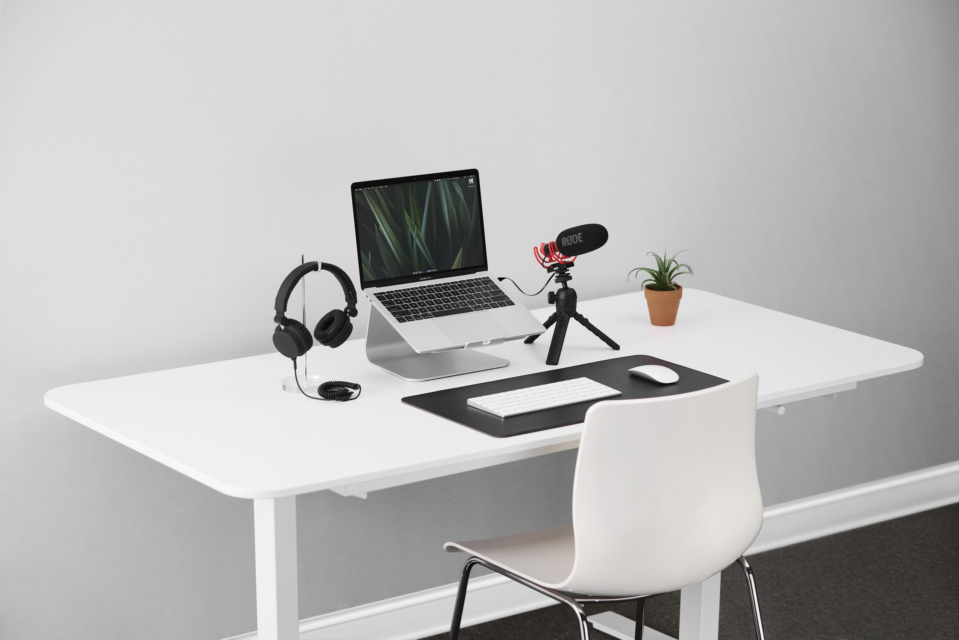 Configurazione scrivania da ufficio con laptop, microfono, cuffie e altri accessori. Sfondo bianco.