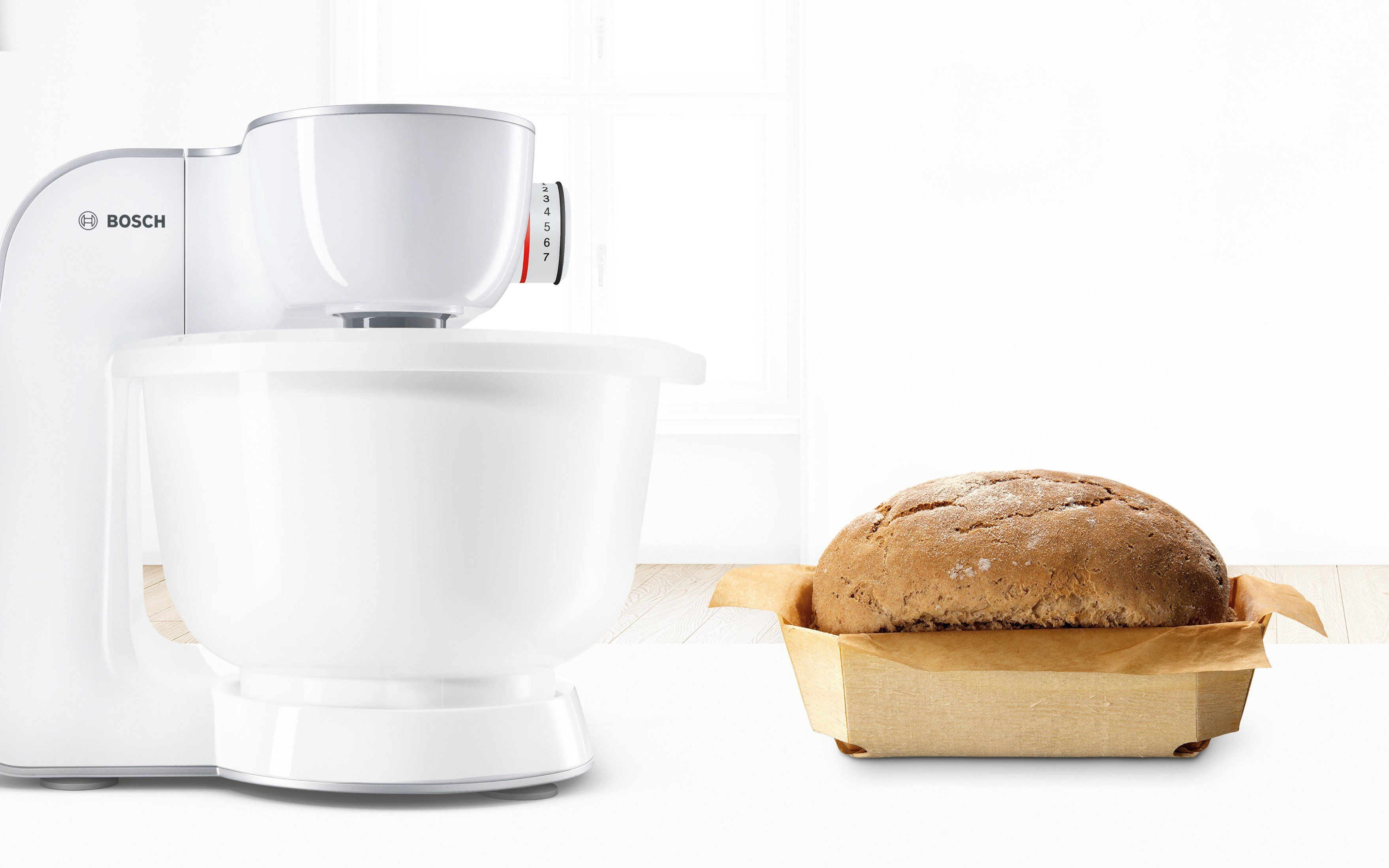 Biała maszyna kuchenna Bosch z misą i bochenkiem chleba w drewnianym koszu.