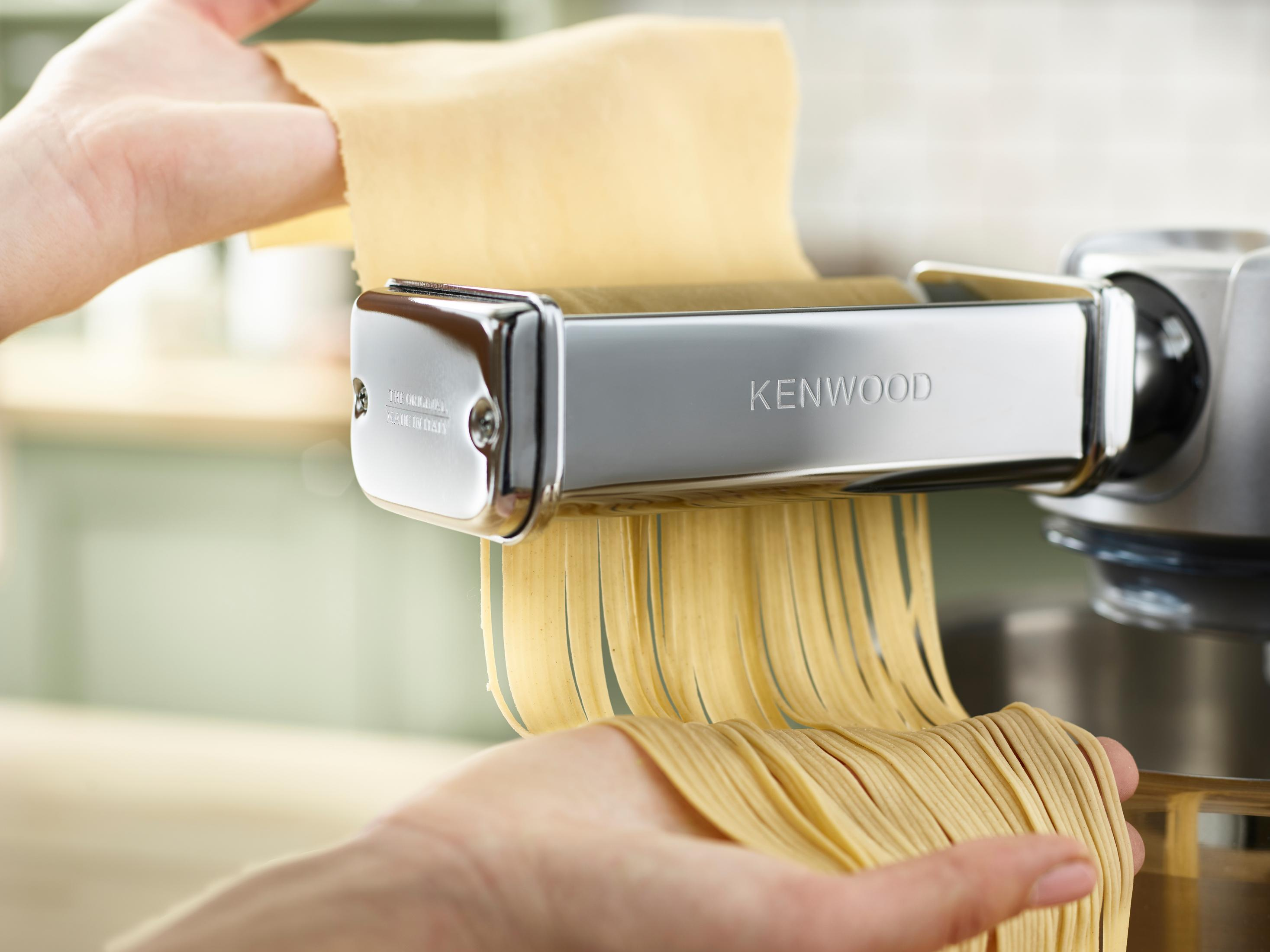 Maszyna do makaronu w użyciu, ręce wyciągają świeże spaghetti, ze srebrną maszyną.