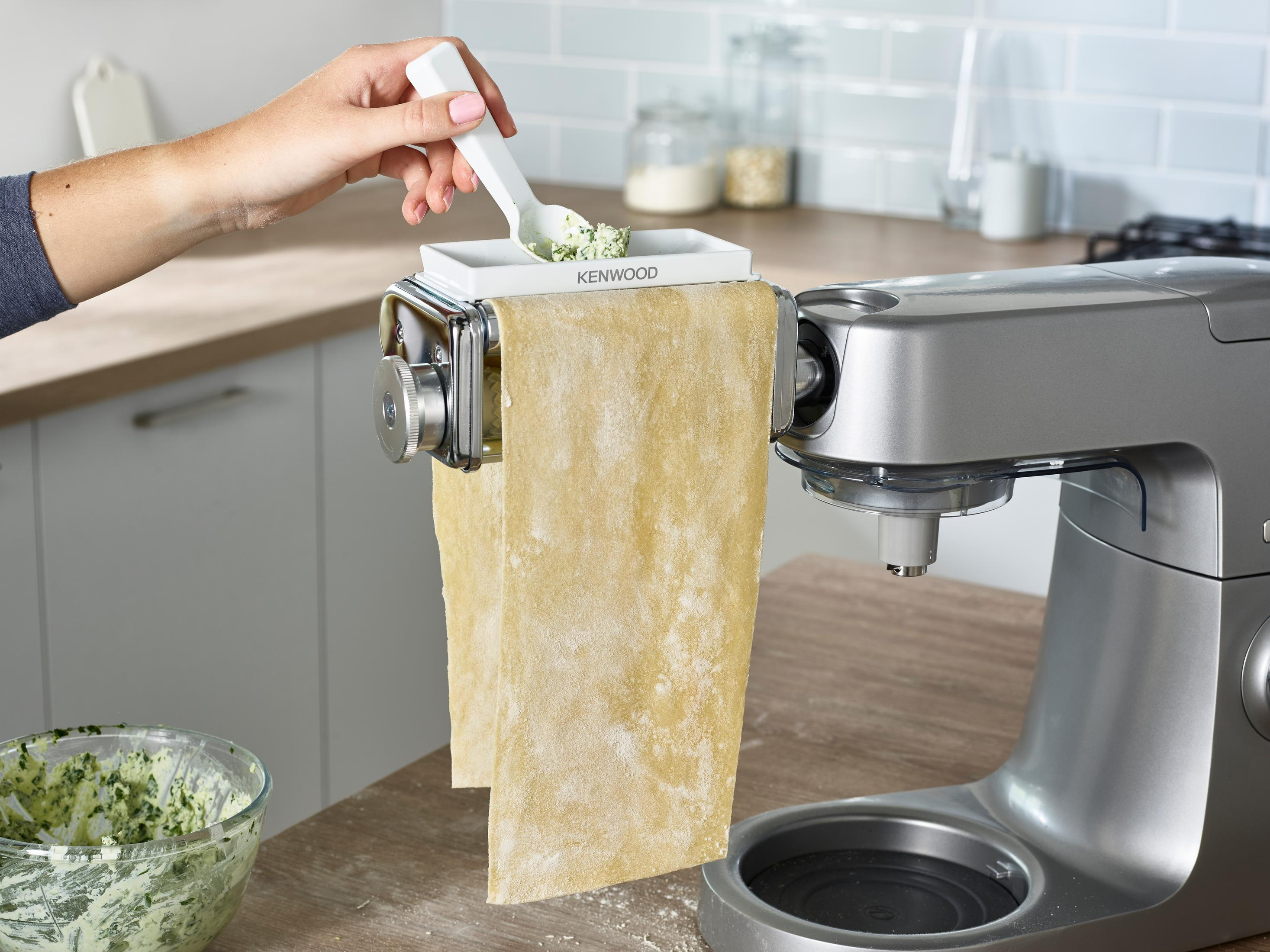 Osoba używająca maszynki do makaronu Kenwood z widocznym ciastem i pesto.