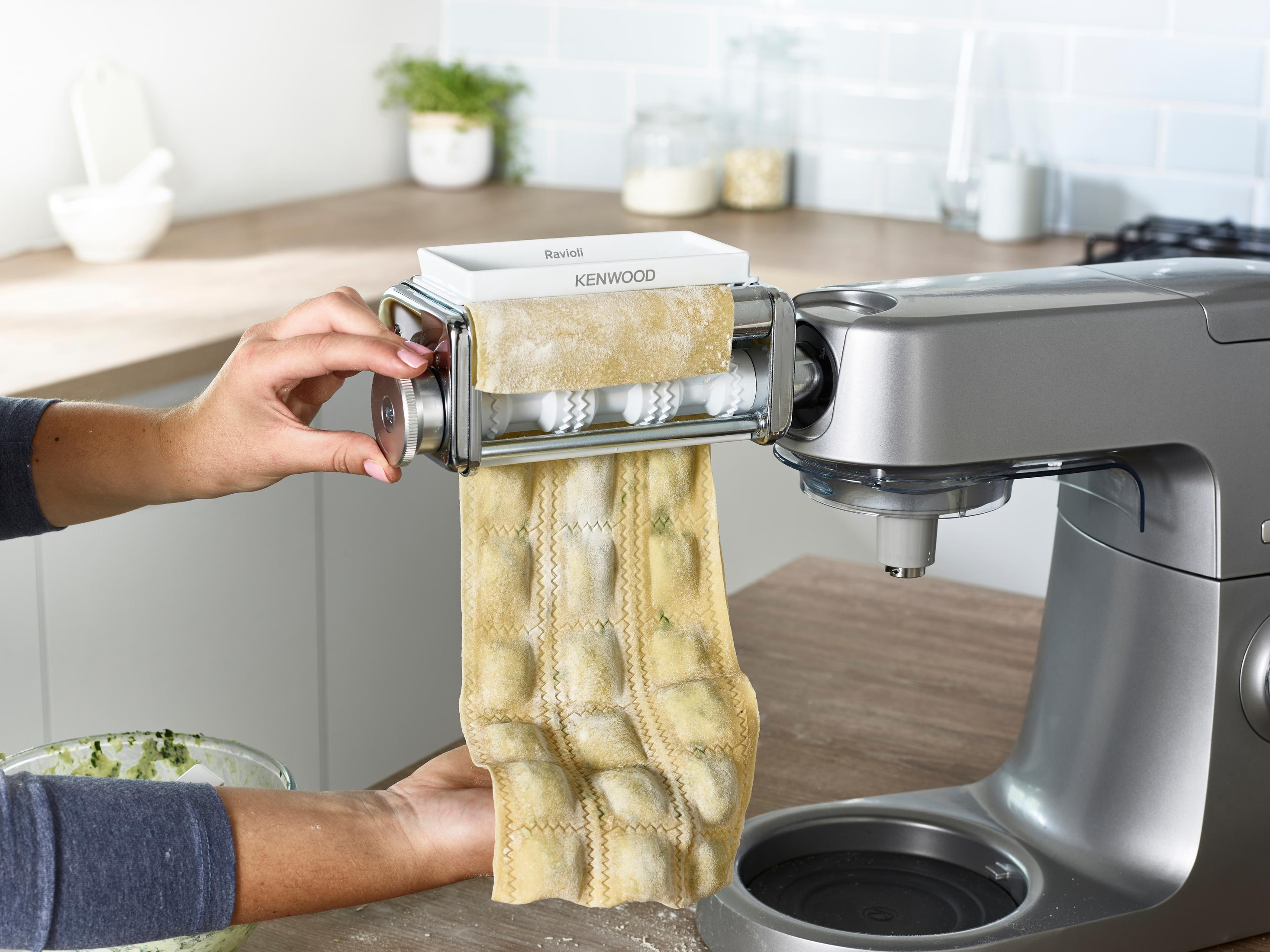 Kobieta robi ravioli za pomocą maszyny do makaronu. Ravioli umieszczone na stole. Srebrna maszyna.