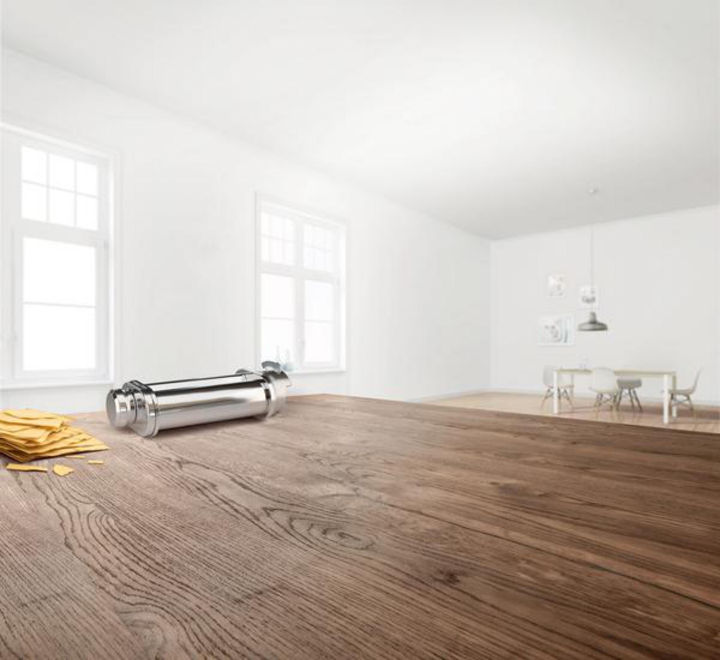 Chrom-Nudelmaschine auf Holztisch. Nudelstapel links. Weißer Raum und Fenster.