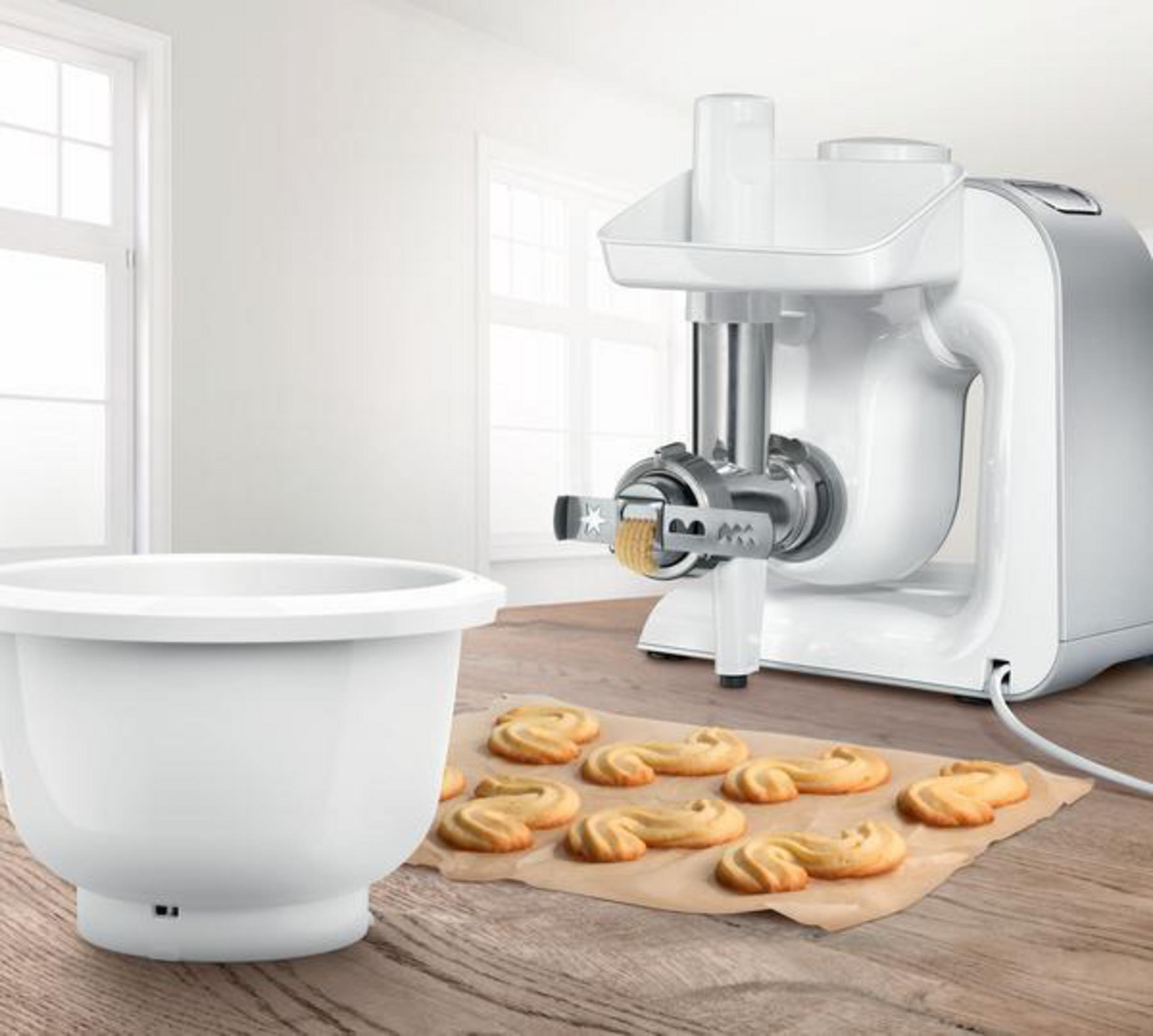 Procesador de alimentos blanco, tazón y galletas en papel pergamino. Superficie de madera.