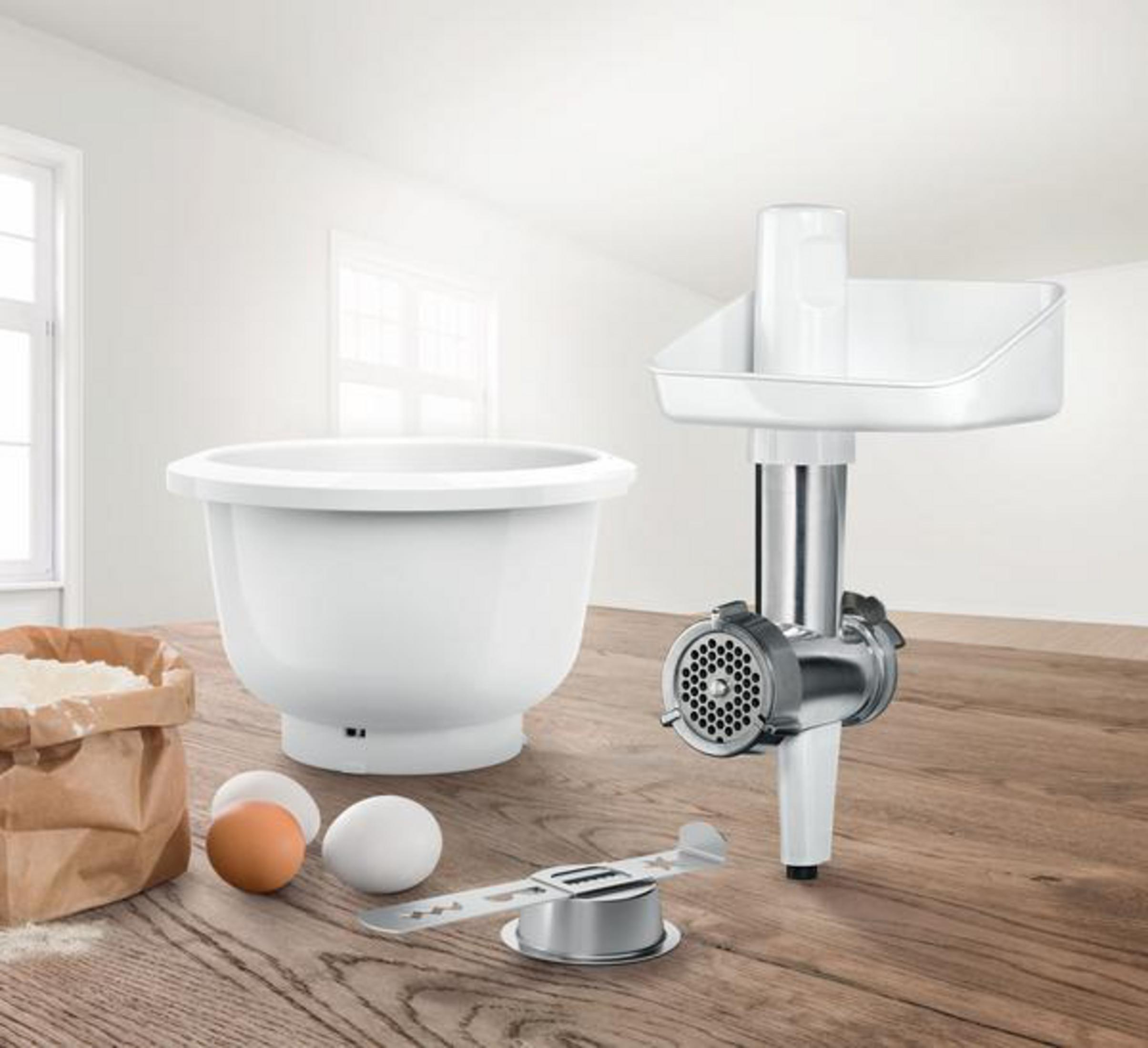 Un electrodoméstico de cocina blanco con un cuenco mezclador, un accesorio de picadora de alimentos e ingredientes.