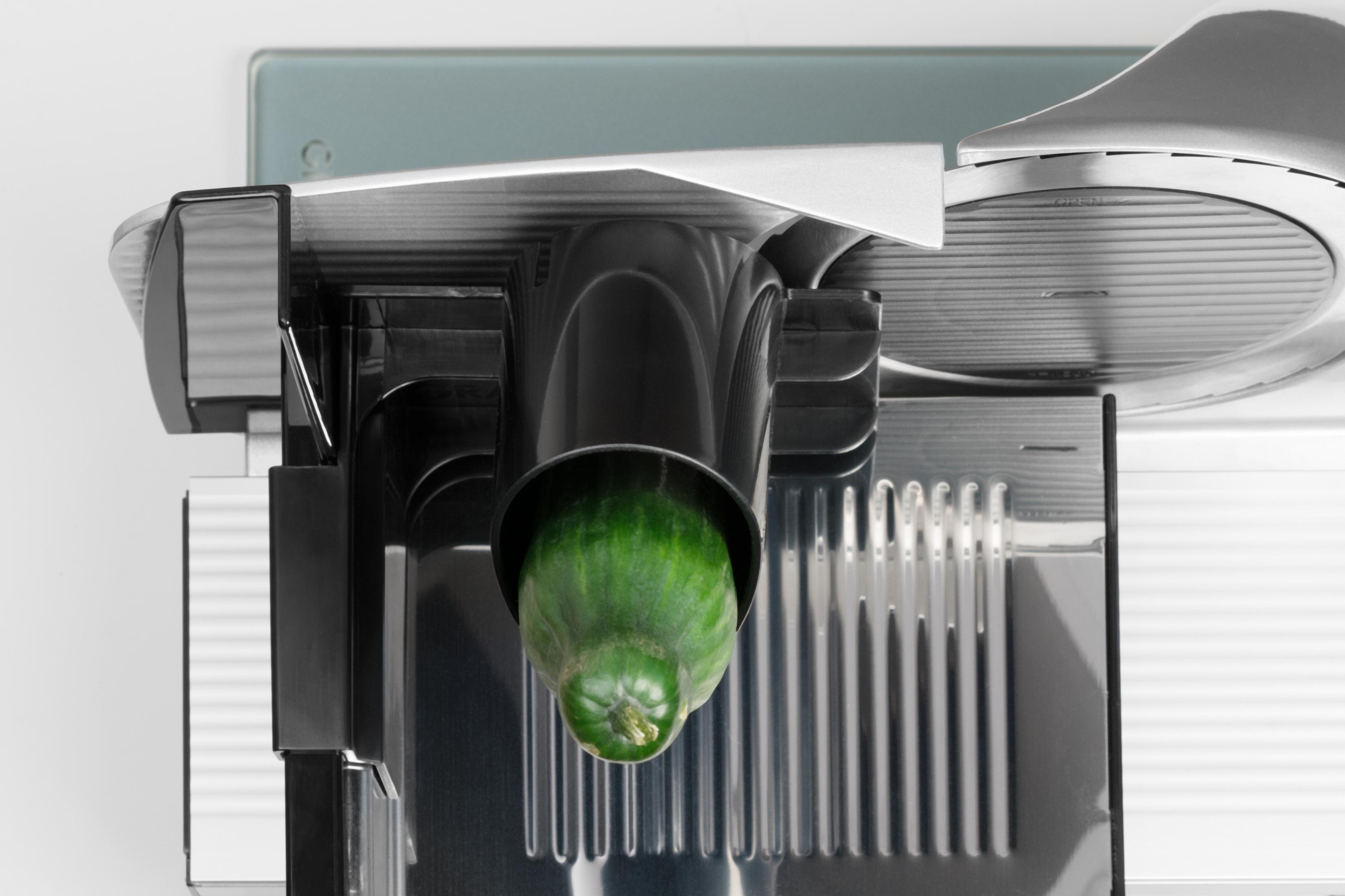 Eine grüne Gurke wird von einer Schneidemaschine geschnitten. Schwarz und Silber.