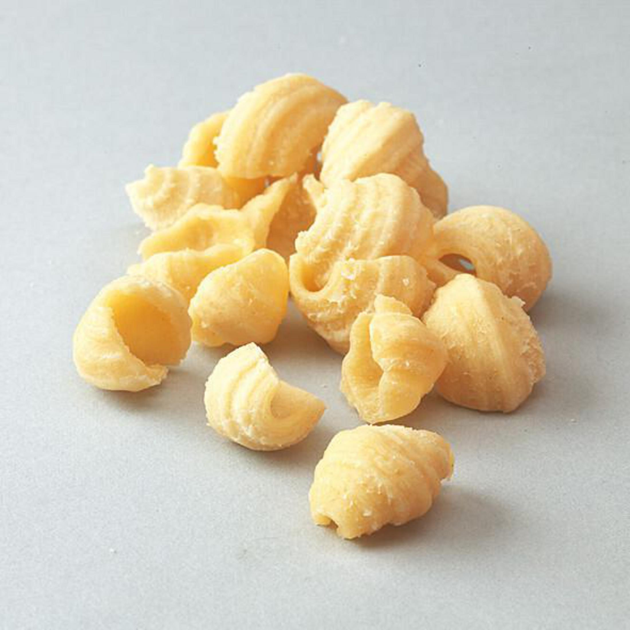 Ein Haufen muschelförmiger Nudeln auf einer hellen Oberfläche. Die Nudeln sind hellgelb.