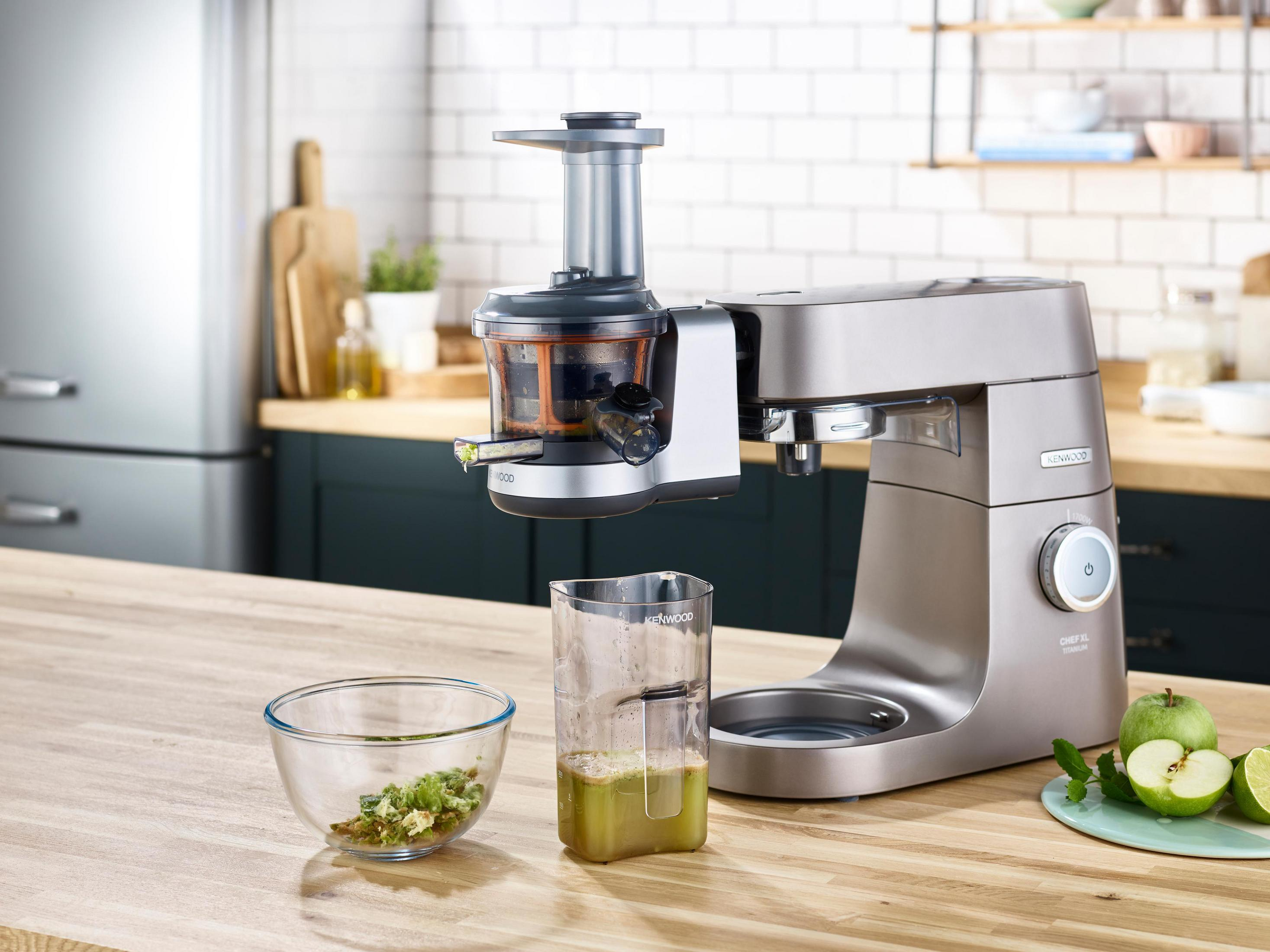 Scena kuchenna z wyciskarką do soku, blenderem, miską posiekanej zieleni i miarką z sokiem.