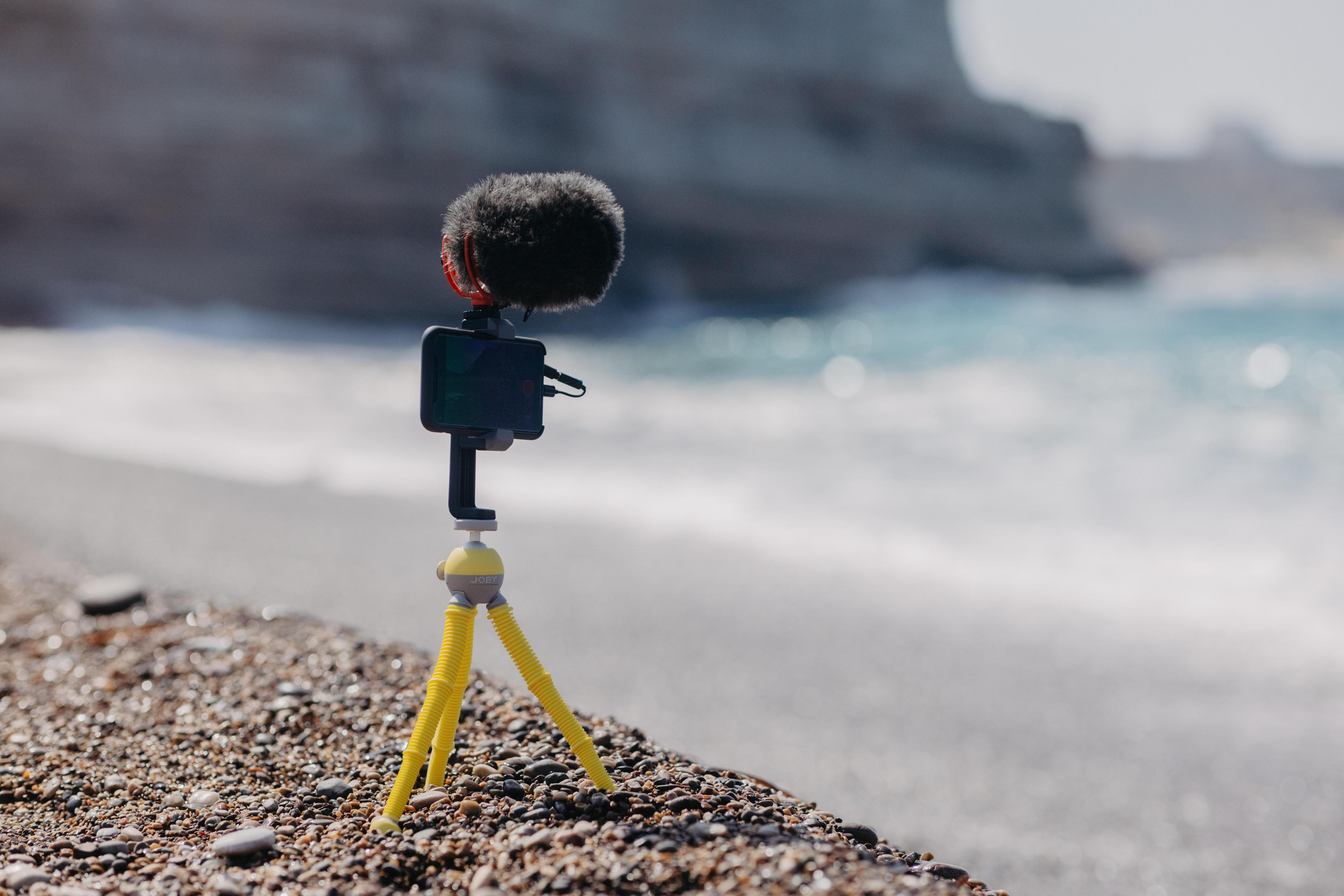 Un trípode amarillo con un micrófono en una playa. El mar está al fondo.