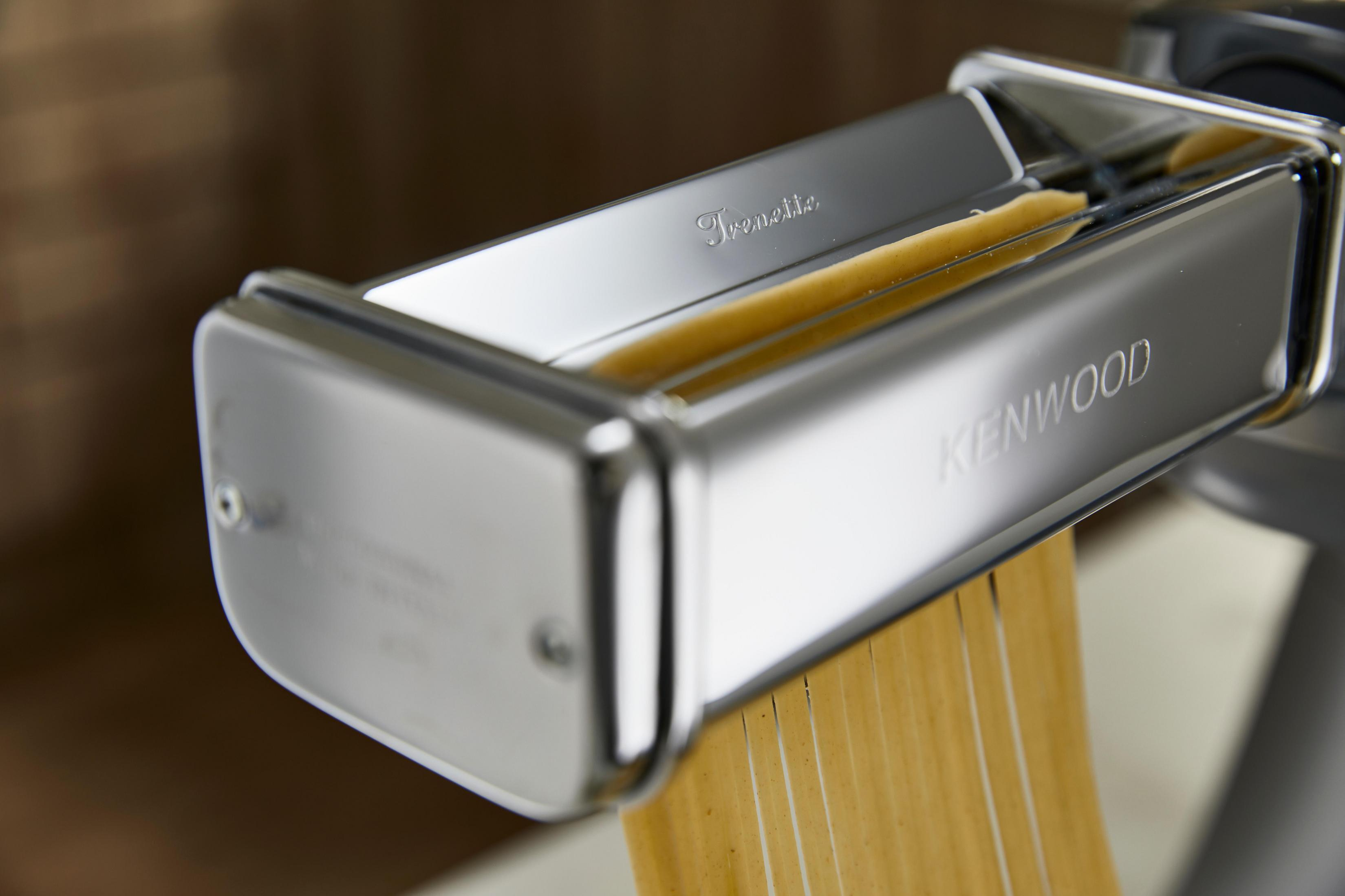 Srebrna maszynka do makaronu Kenwood z wychodzącymi wstążkami makaronu. Makaron jest beżowy, zbliżenie.