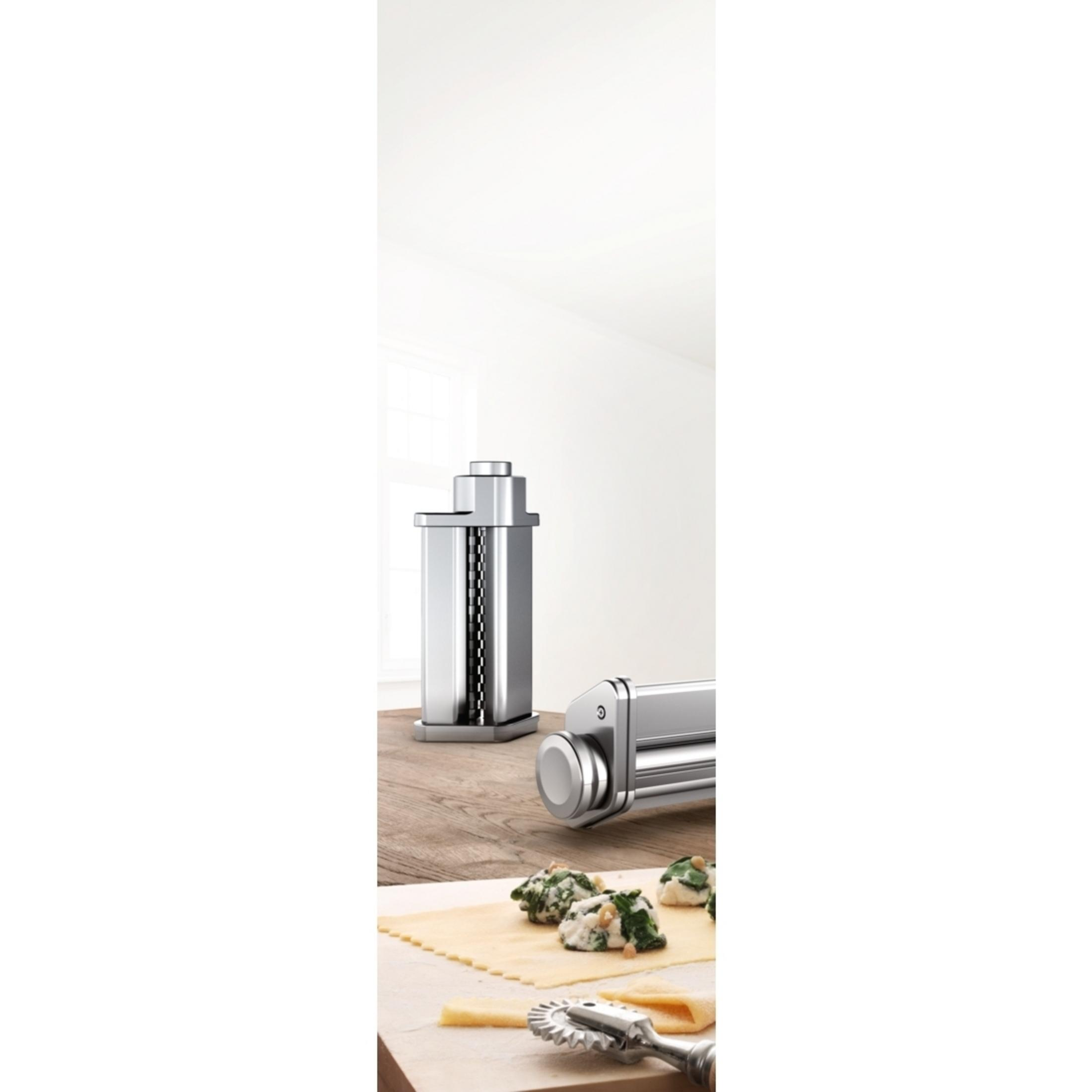 Maszyna do makaronu na drewnianym stole. Widoczne są dwie części maszyny z makaronem i nożem.