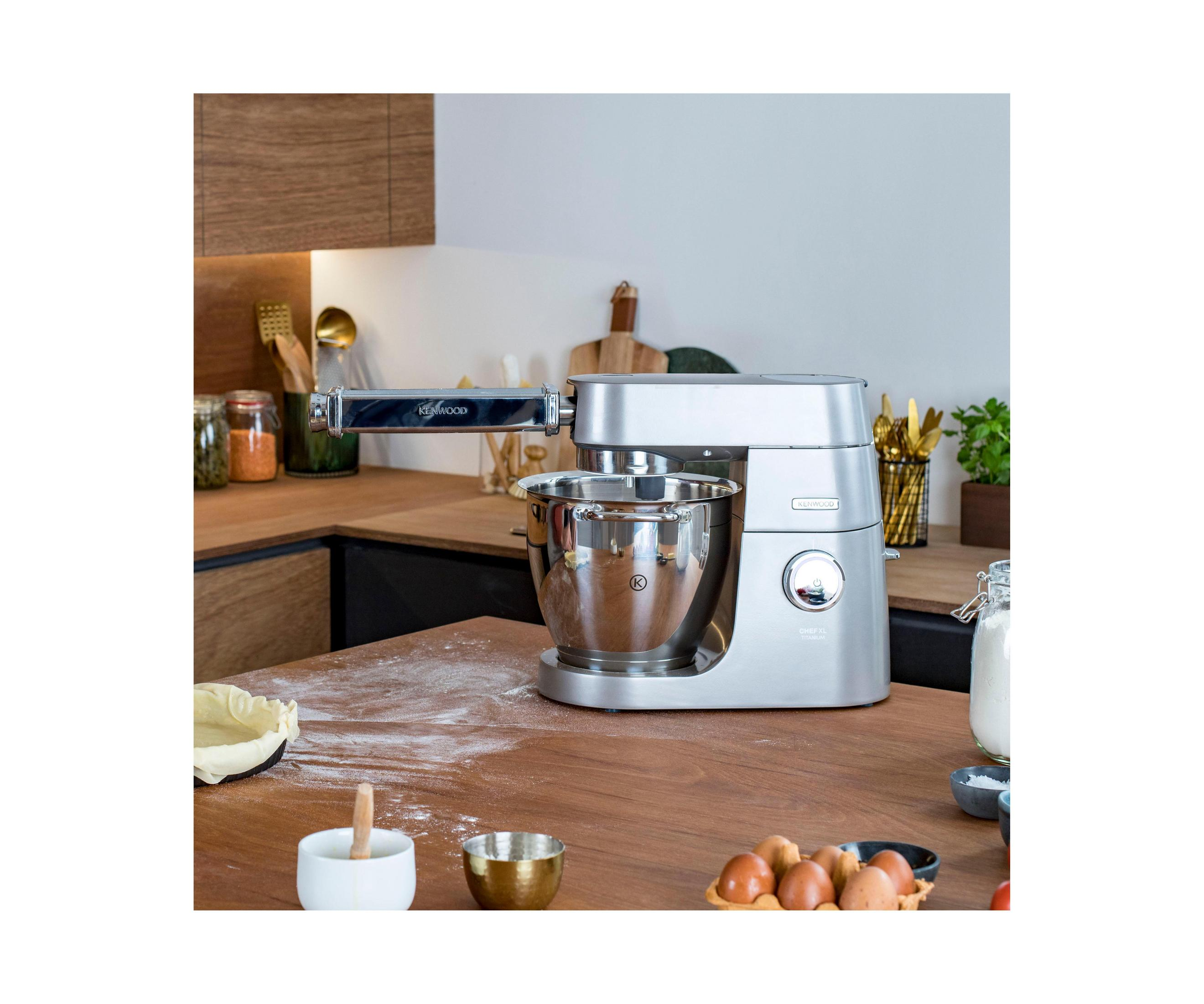 Srebrna maszyna kuchenna Kenwood na drewnianej powierzchni ze składnikami i przyborami.