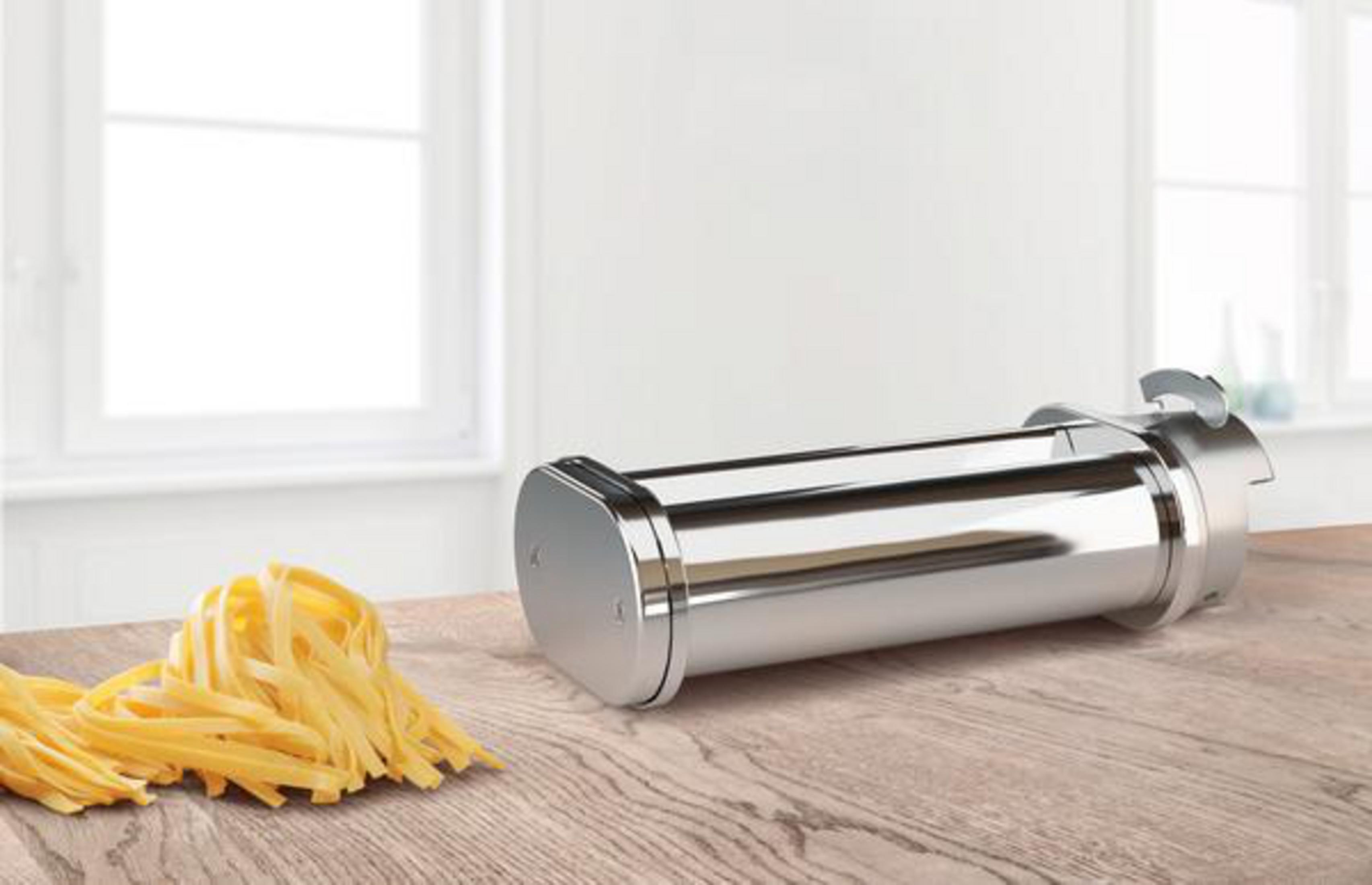 Una máquina de pasta con un montón de pasta fresca sobre una mesa de madera, sobre un fondo blanco.