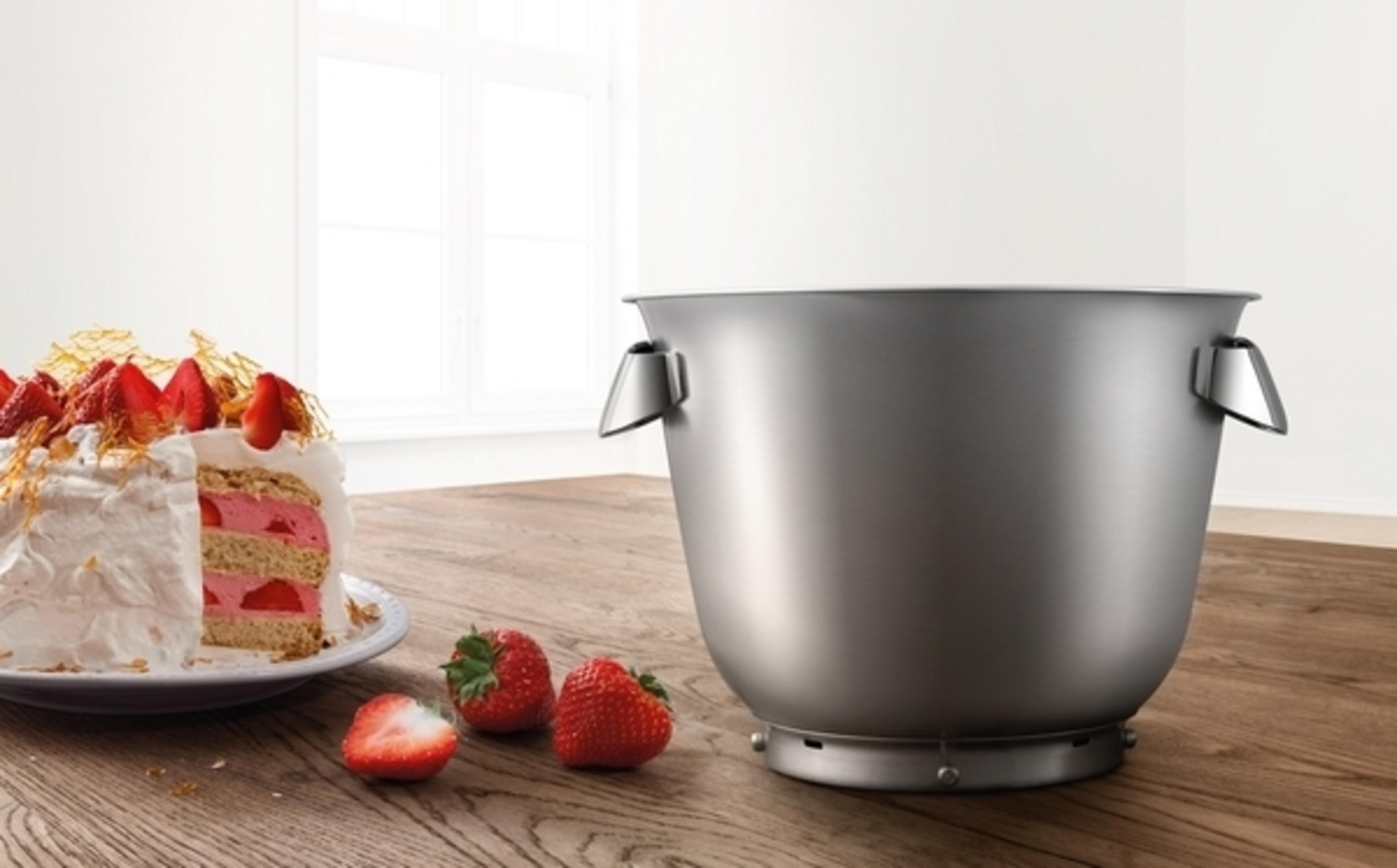 Edelstahl-Rührschüssel mit Kuchen und Erdbeeren auf einem Holztisch. Weißer Hintergrund.