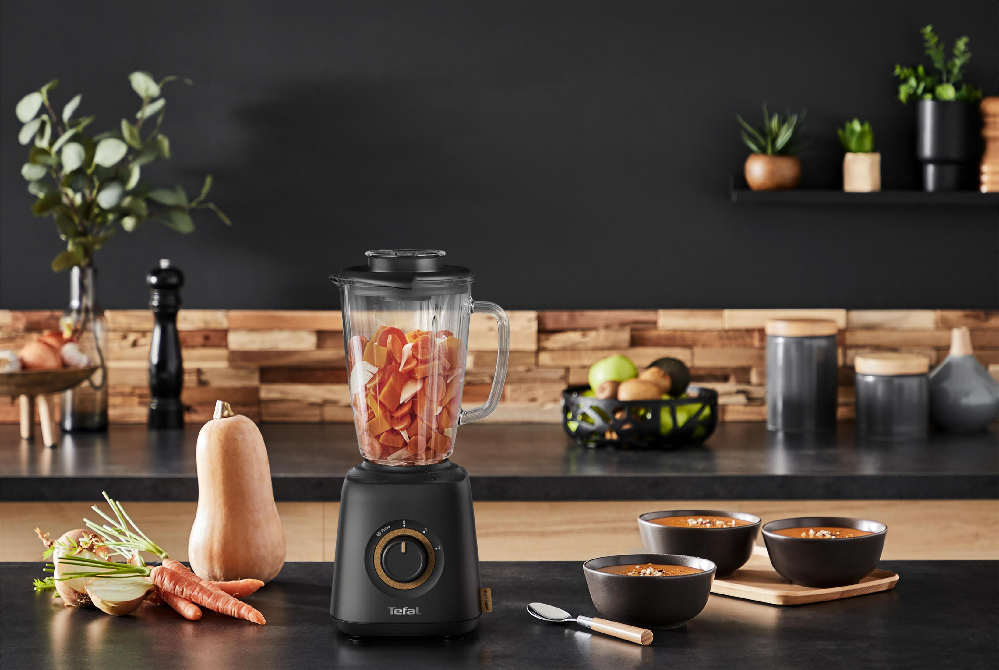 Schwarzer Mixer mit Glasbehälter voller Apfelscheiben und zwei Schüsseln Suppe.