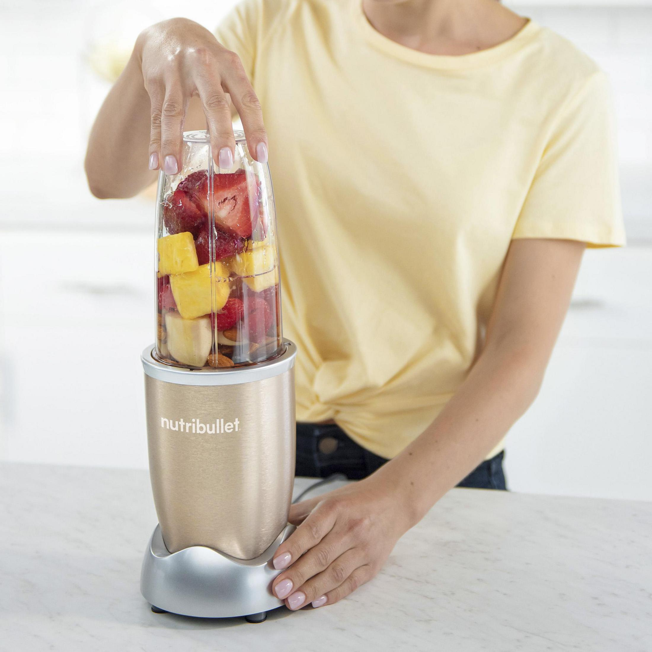 Una persona tiene in mano un frullatore NutriBullet con frutta all'interno. Il frullatore è su un piano bianco.