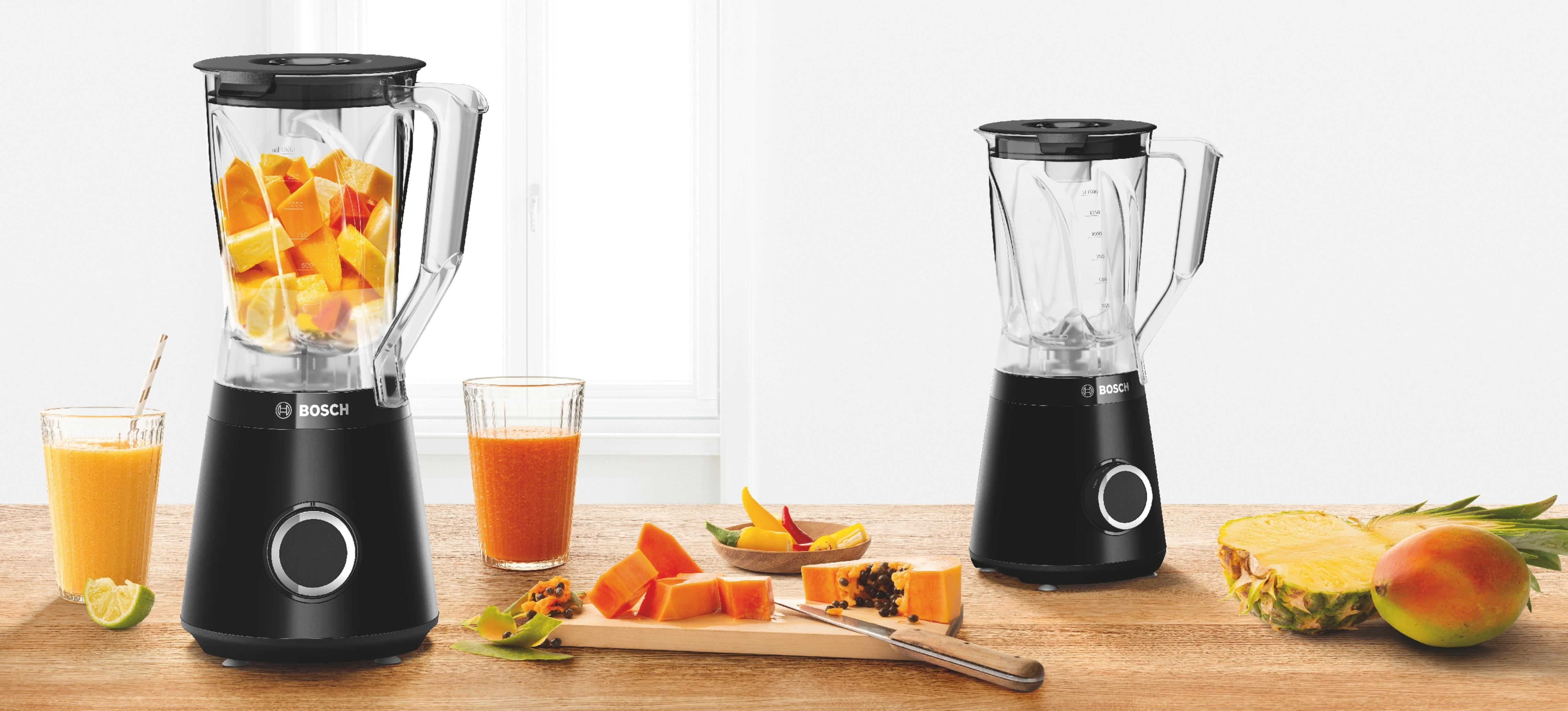 Dwa czarne blendery Bosch, jeden wypełniony owocami, na stole z owocami i napojami.