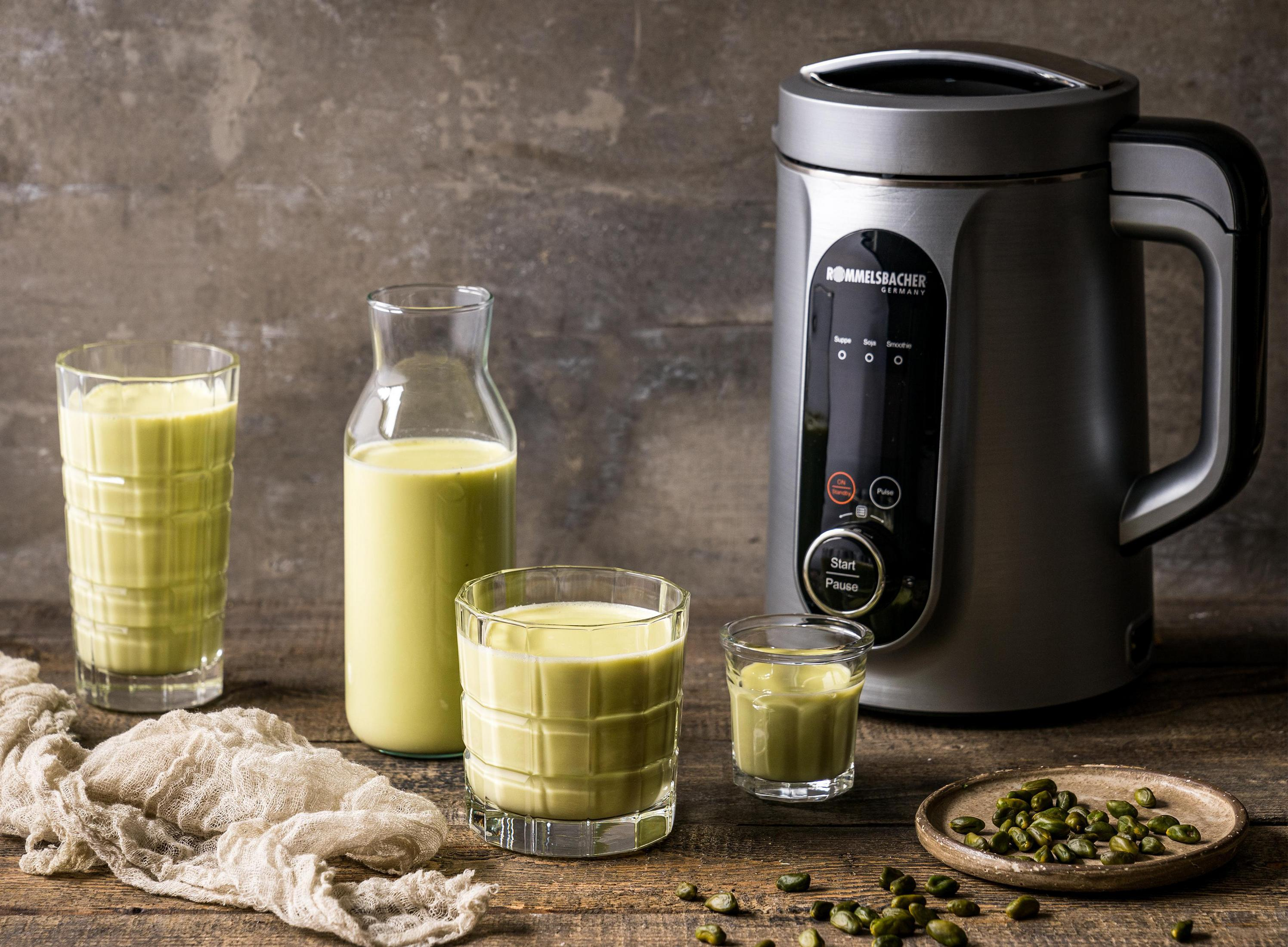 Ein Smoothie-Maker mit Gläsern grünen Smoothies, Samen und einem Tuch auf einem Holztisch.