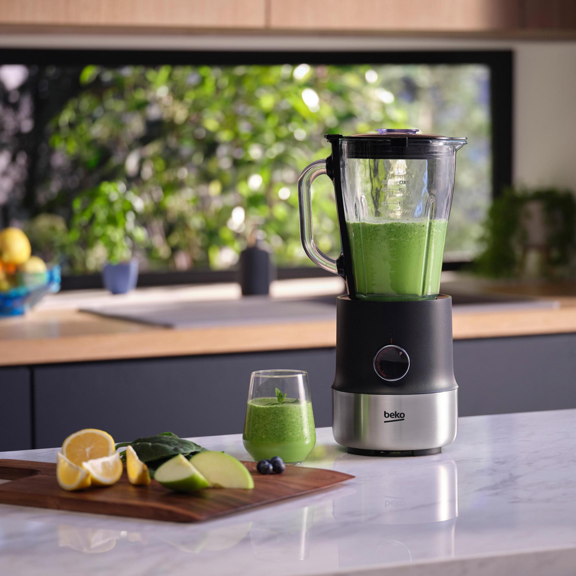 Blender z zielonym koktajlem, plus szklanka koktajlu i składniki na drewnianej desce.