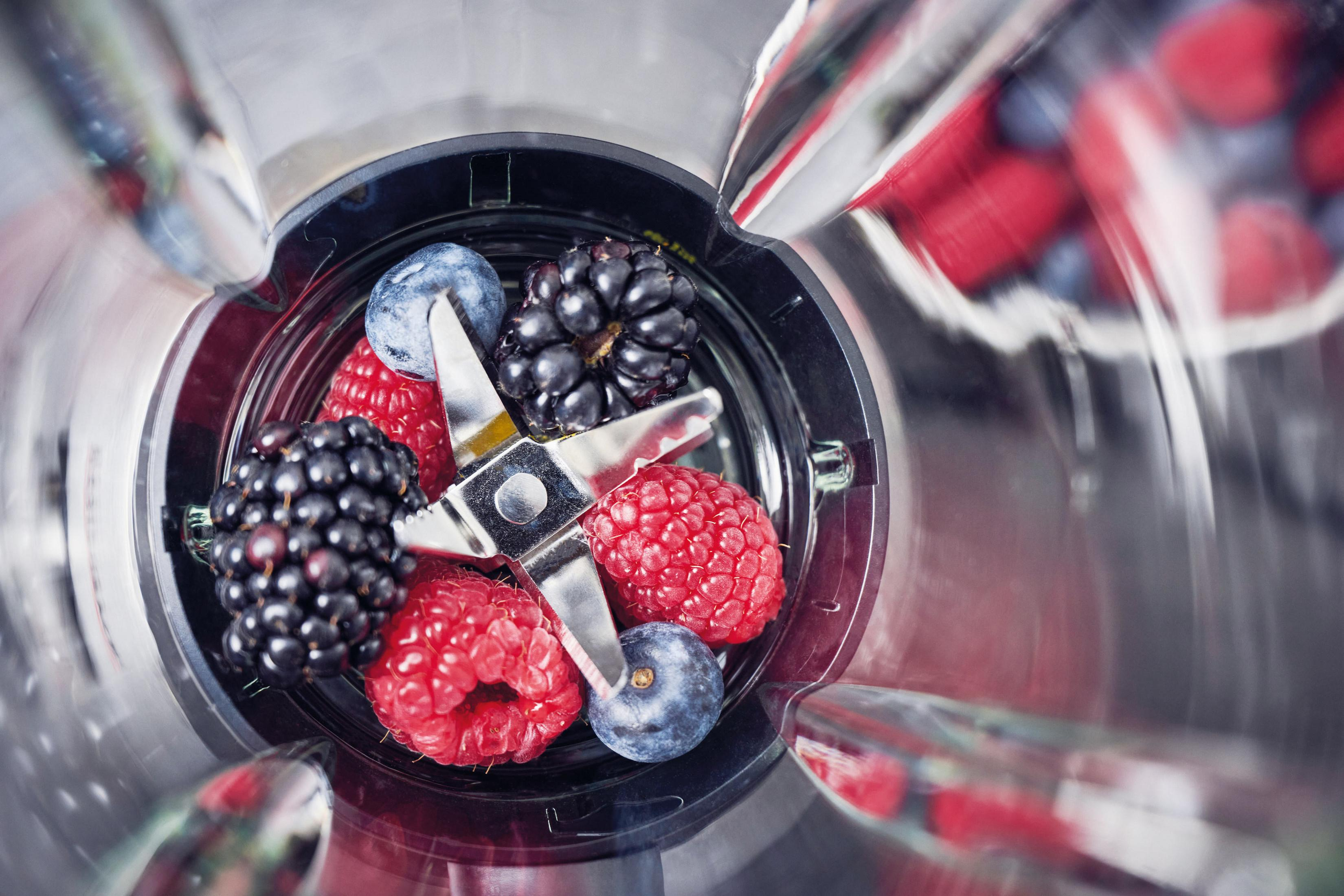 Un frullatore pieno di frutti di bosco, mostra un primo piano della frutta all'interno.