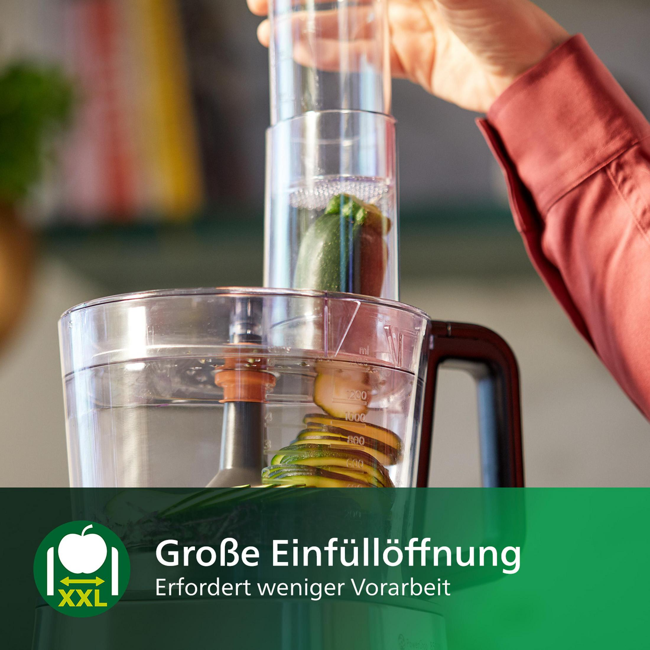 Ein Food-Processor mit Zucchini, die verarbeitet wird. Text auf Deutsch: 'Große Einfüllöffnung'.