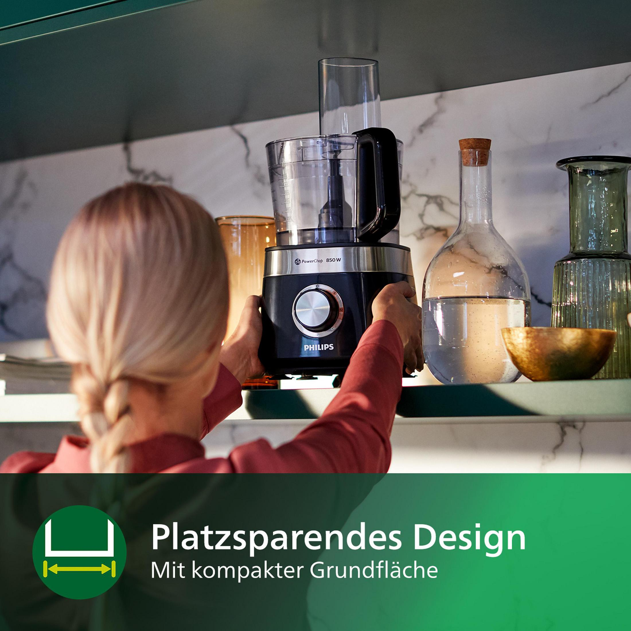 Eine Frau benutzt einen schwarzen Küchenroboter mit einem Glasbehälter auf einem grünen Regal.