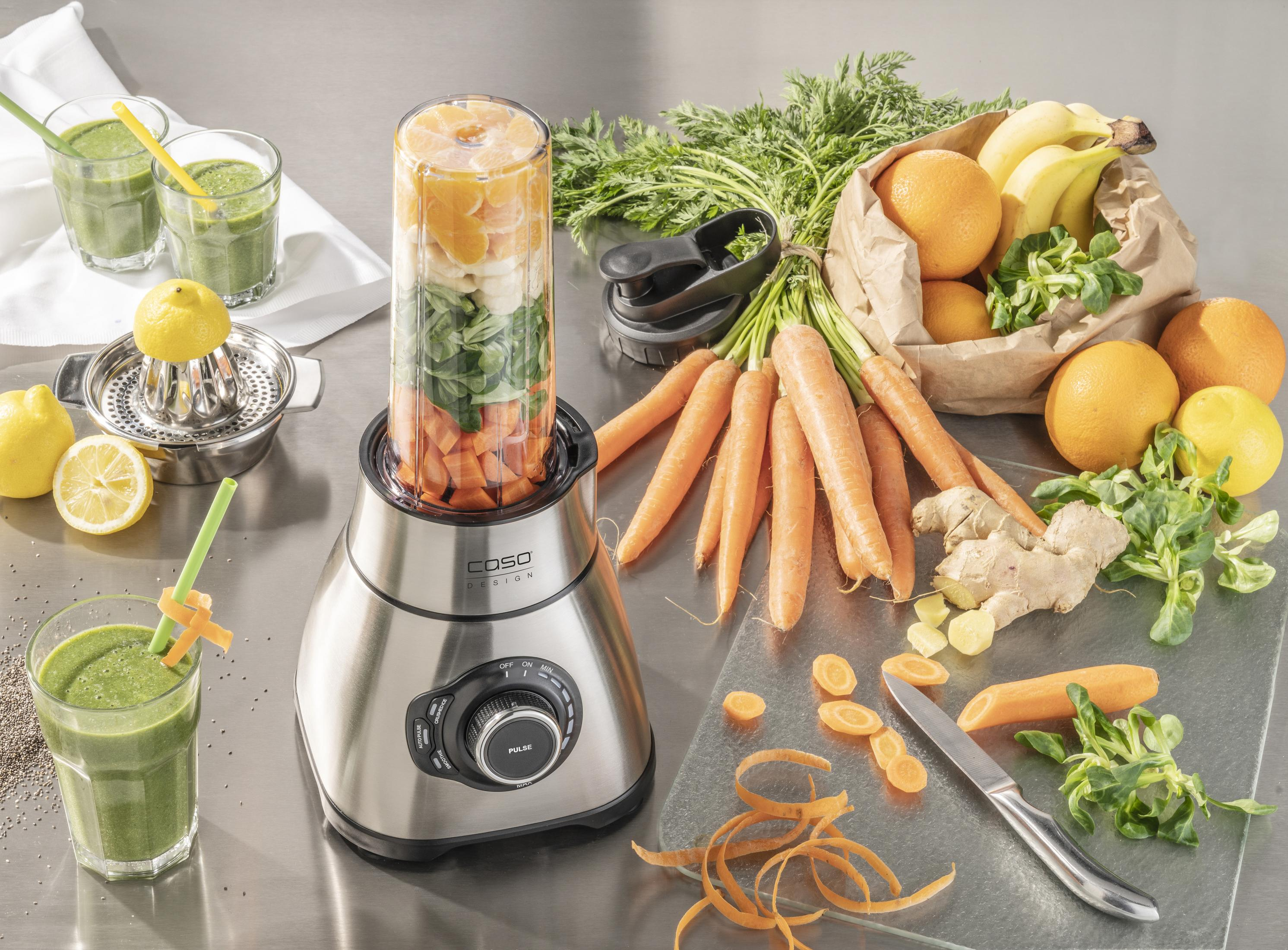 Mixer mit Zutaten. Karotten, Orangen und Zitronen auf dem Tisch, grüner Smoothie im Glas.