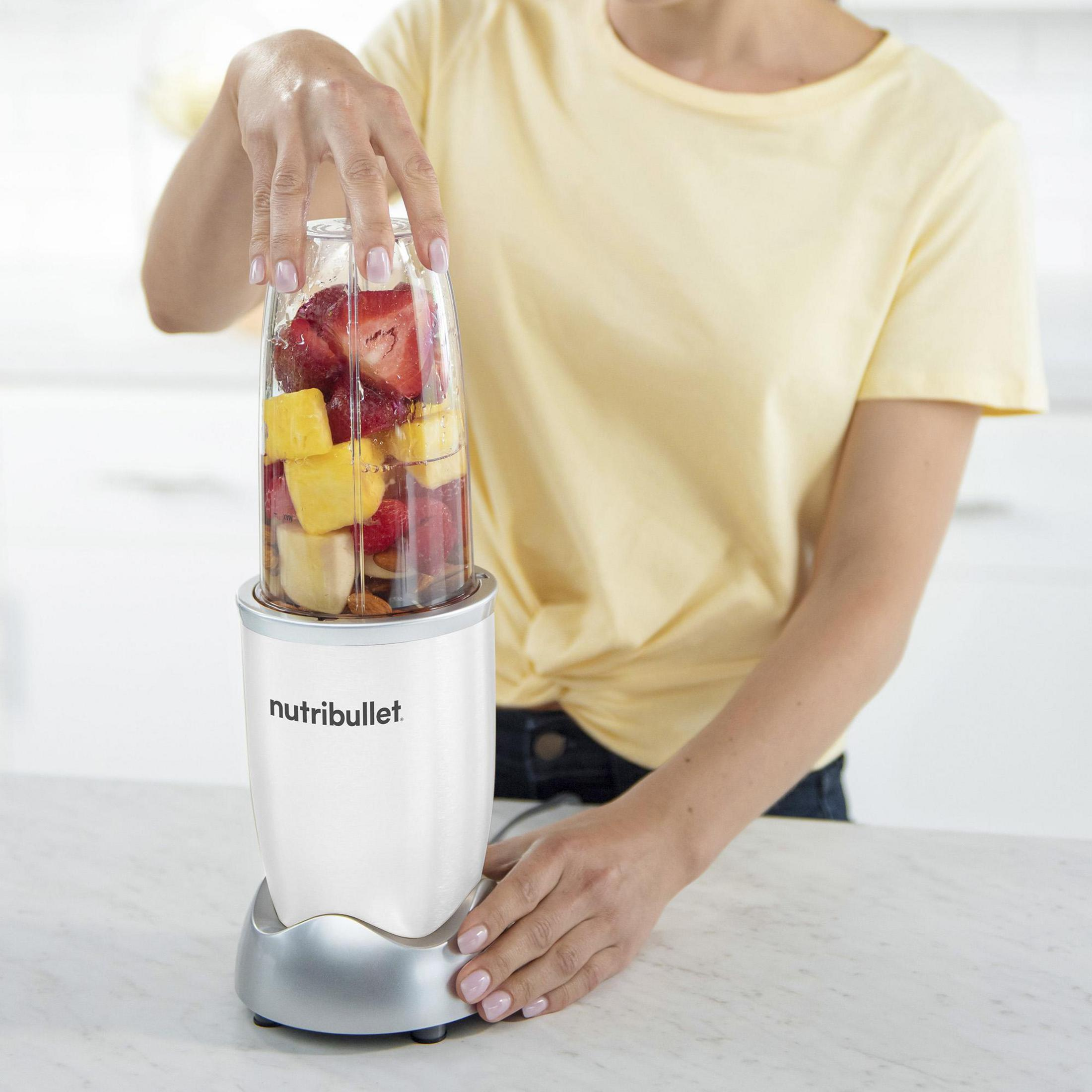Eine Person, die Früchte in einem weißen Nutribullet-Mixer auf einer weißen Oberfläche mixt.