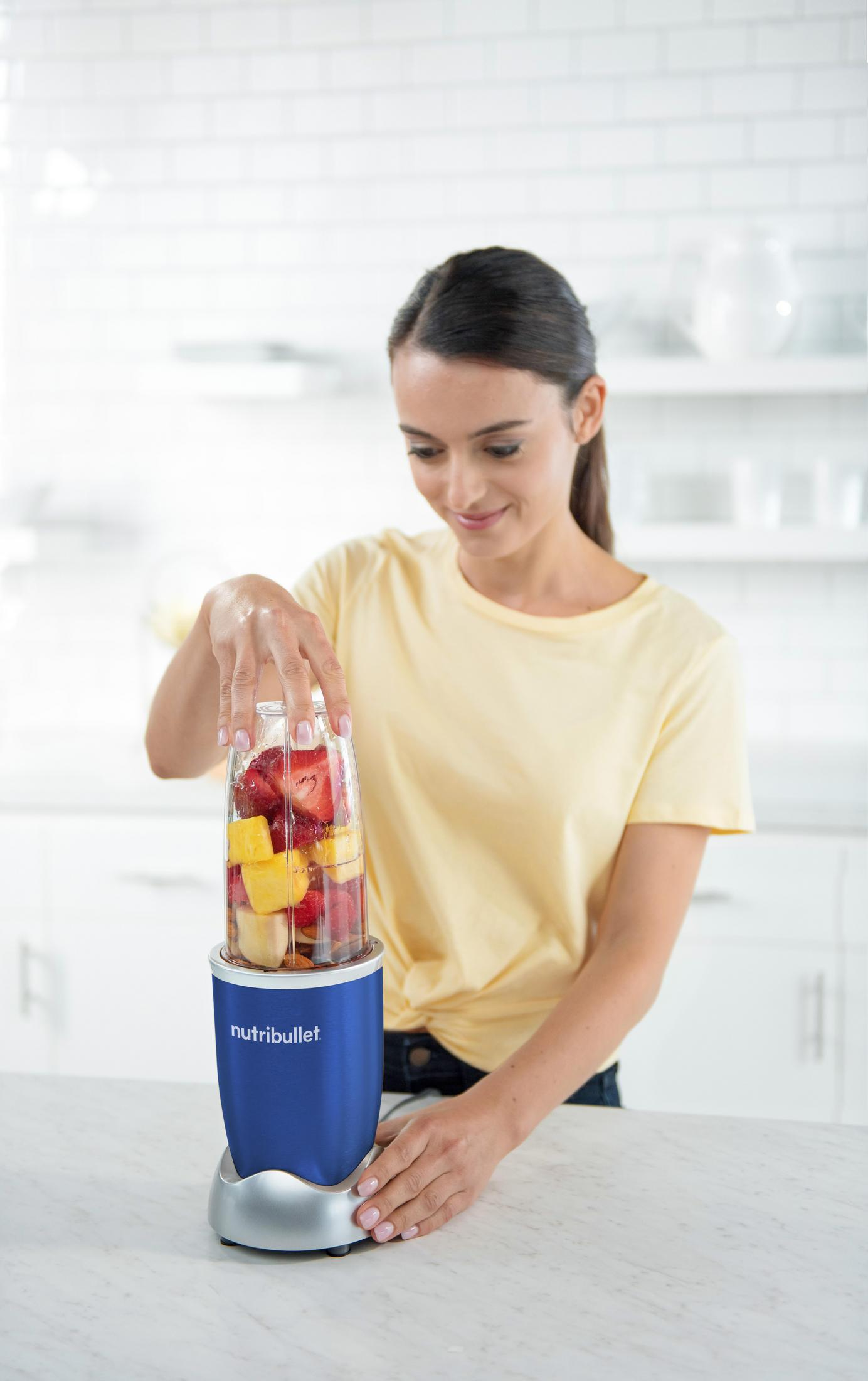 Una donna sta preparando un frullato con un Nutribullet blu. Sta aggiungendo frutta nel frullatore.